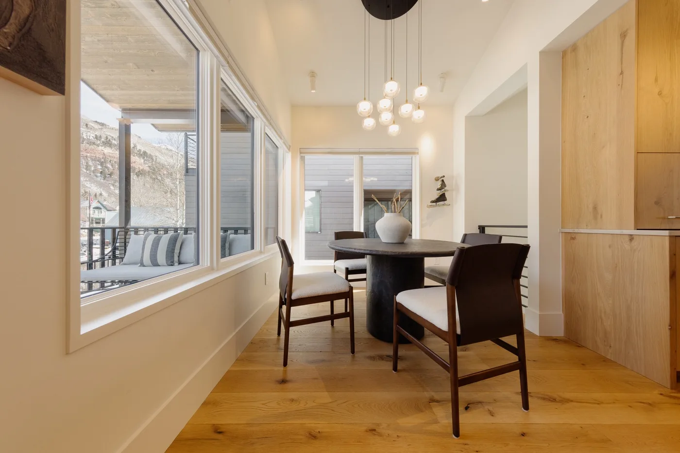 A dining area with a dark table and chairs beside large windows.