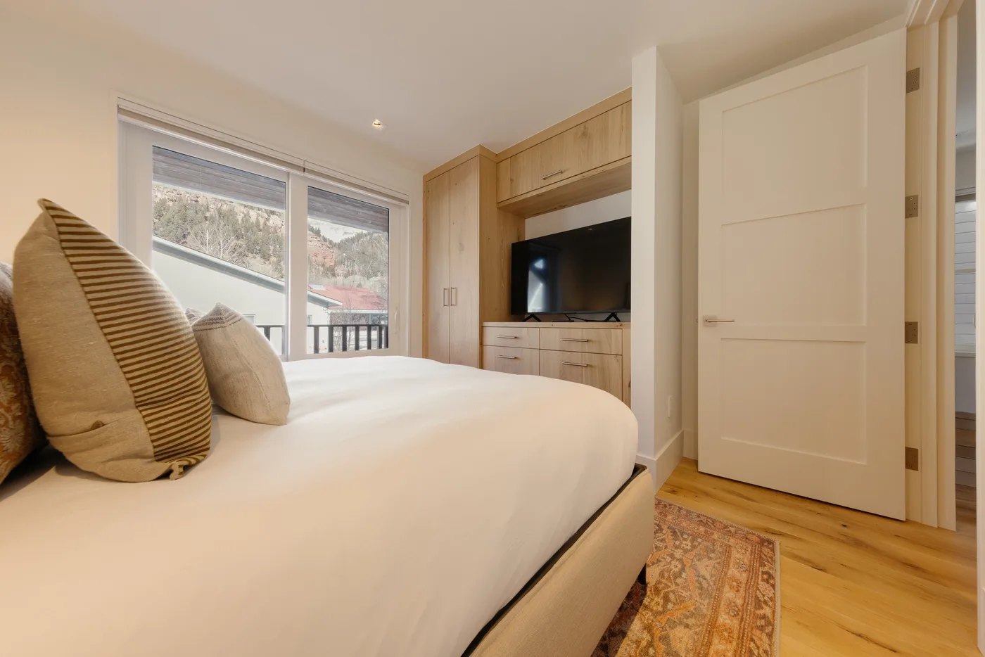 A bedroom with a bed beside a window and a television on a wooden cabinet.