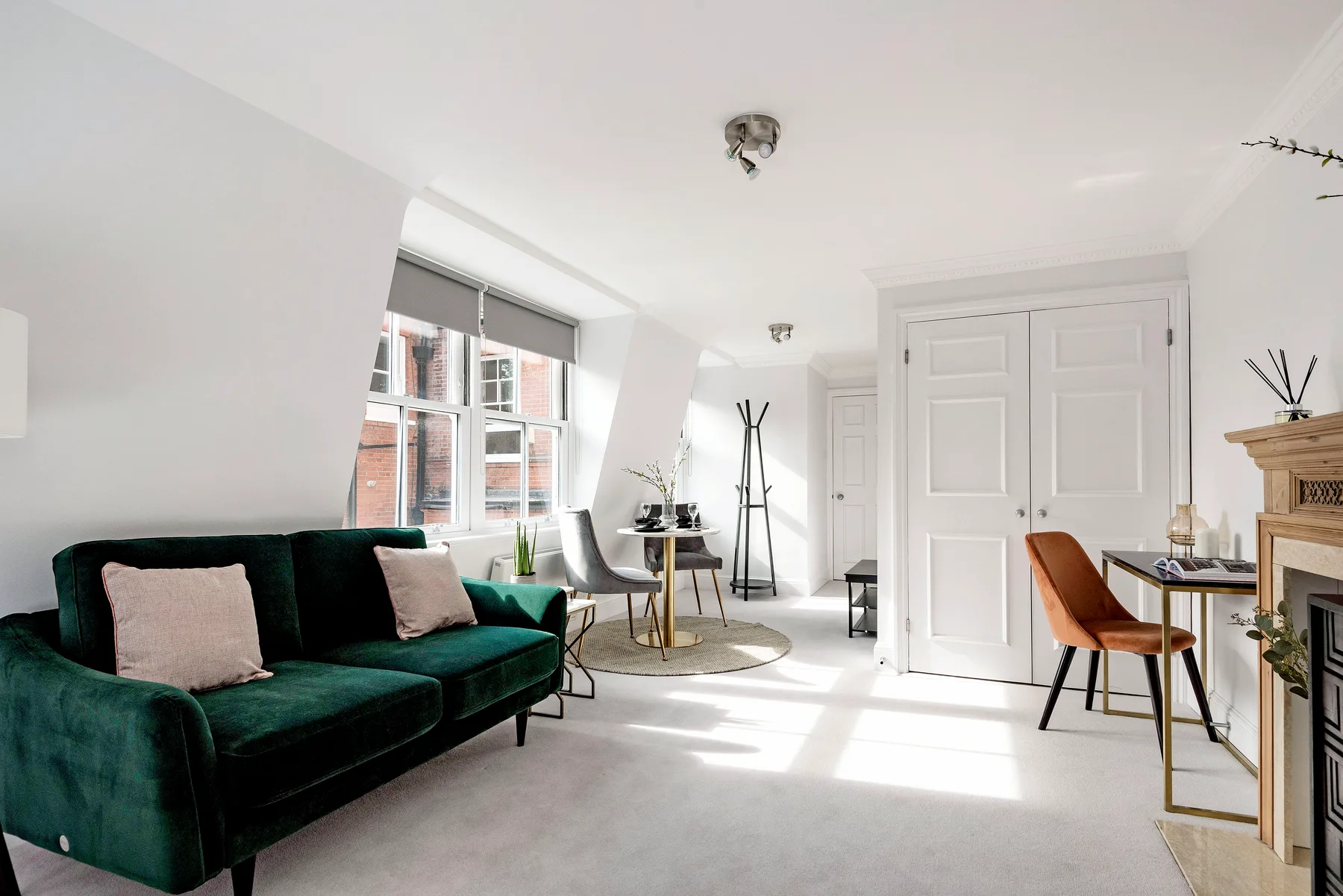A bright living room with green seating and a dining table by the windows.