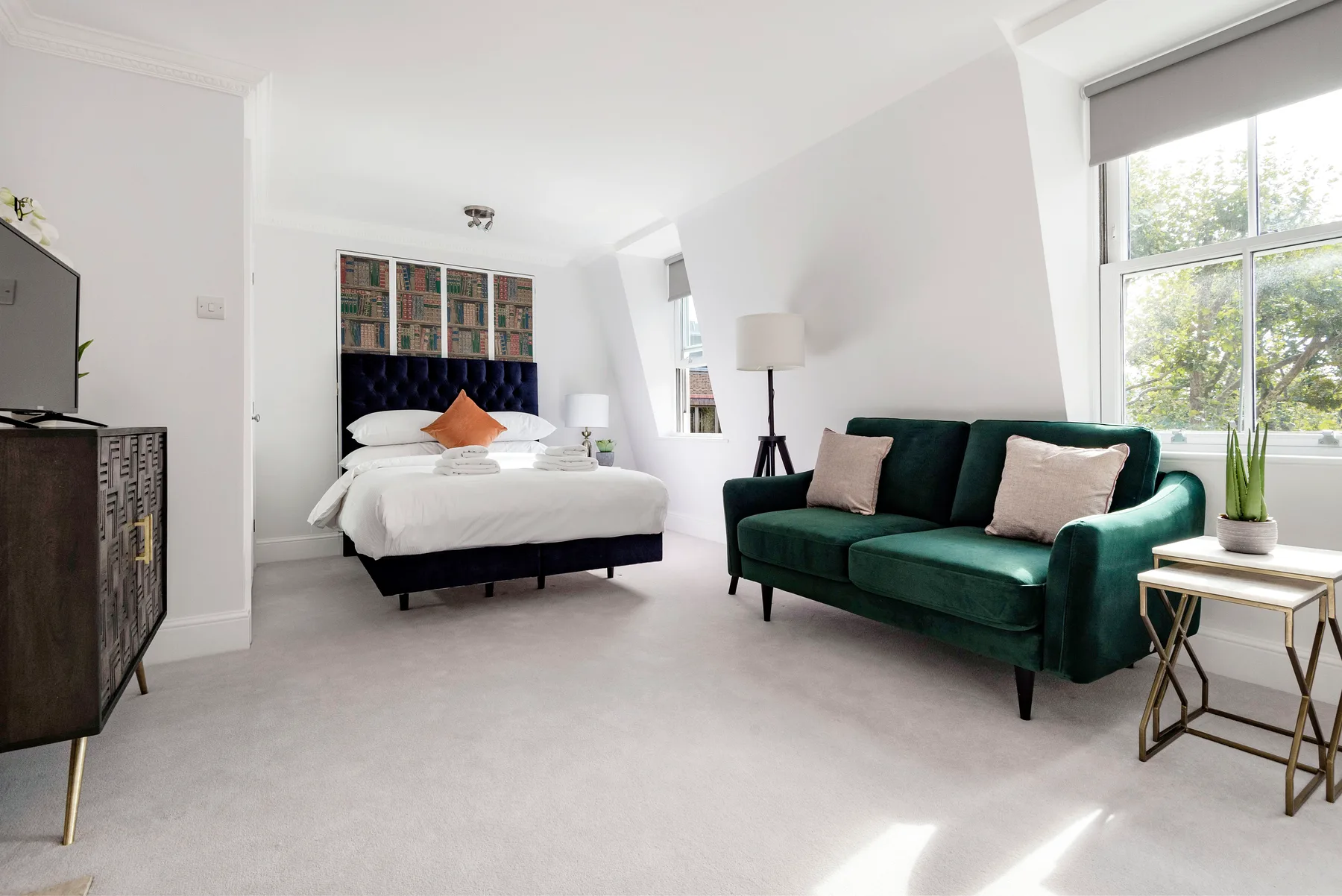 A bright bedroom with a bed, green seating, and large windows.