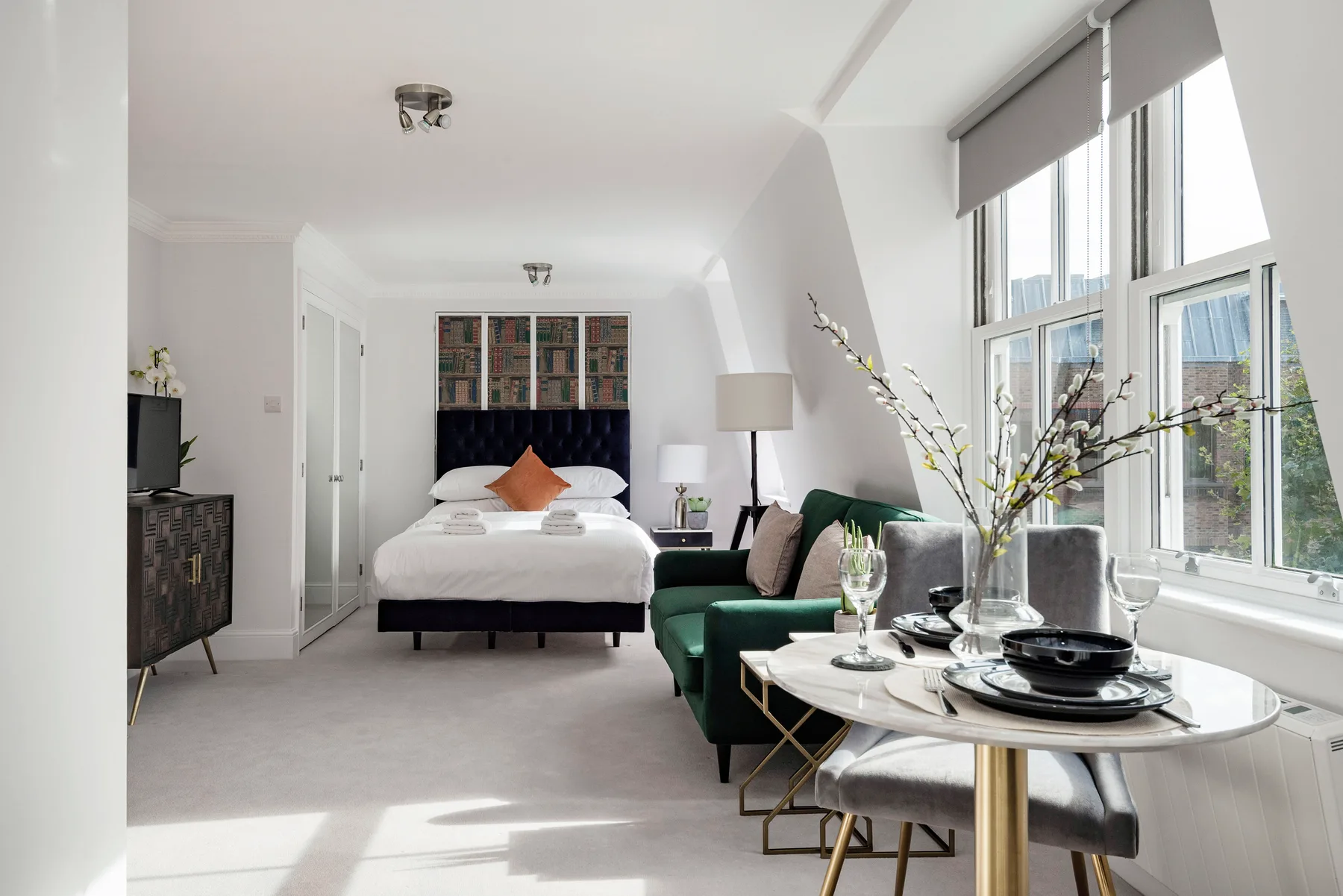 A bright bedroom with a bed, a small dining table, and large windows.