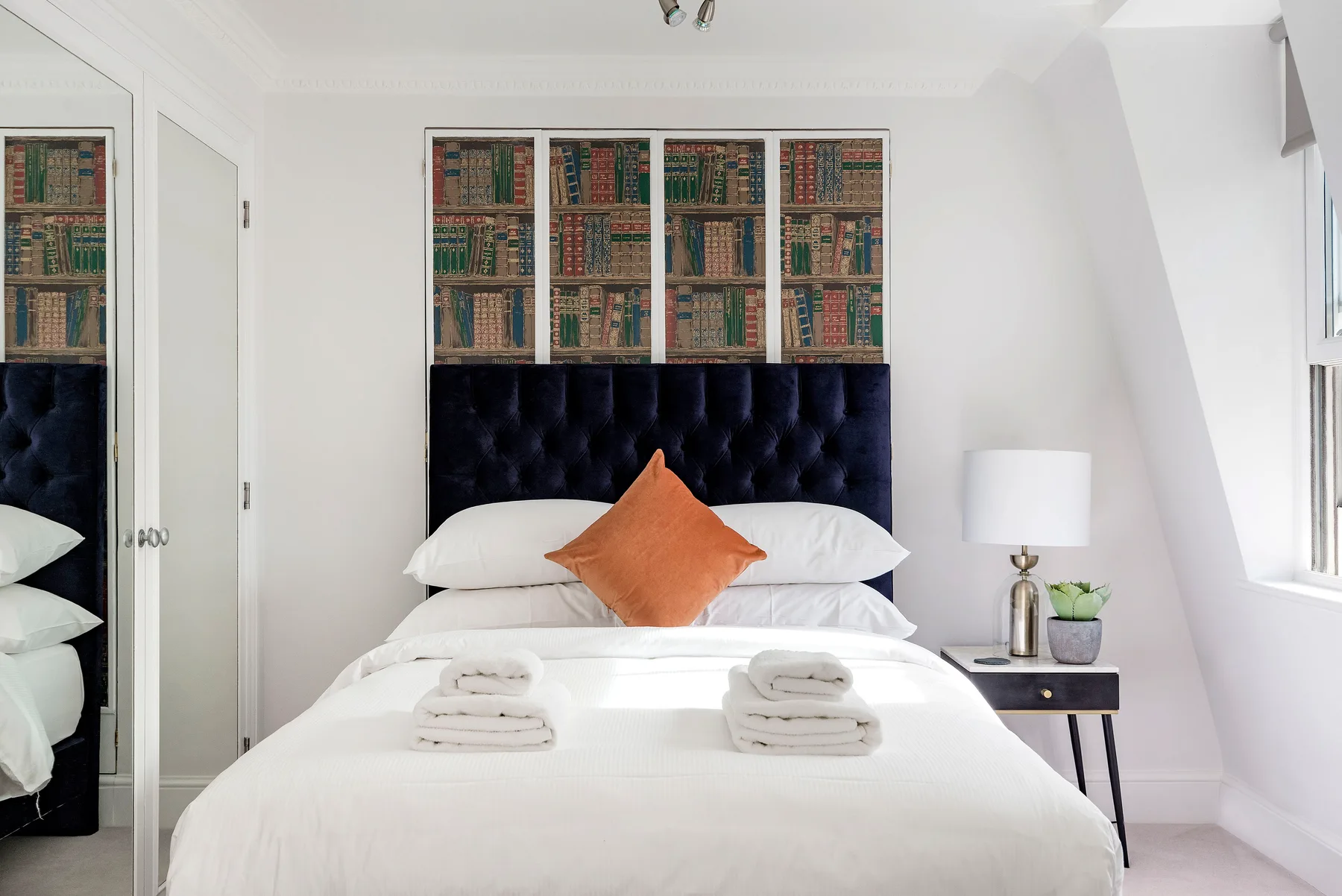 A neatly made bed with white bedding and an orange accent pillow.