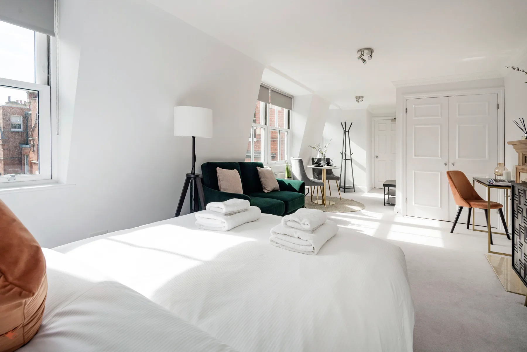 A bright bedroom with a neatly made bed and a dark green seating area.