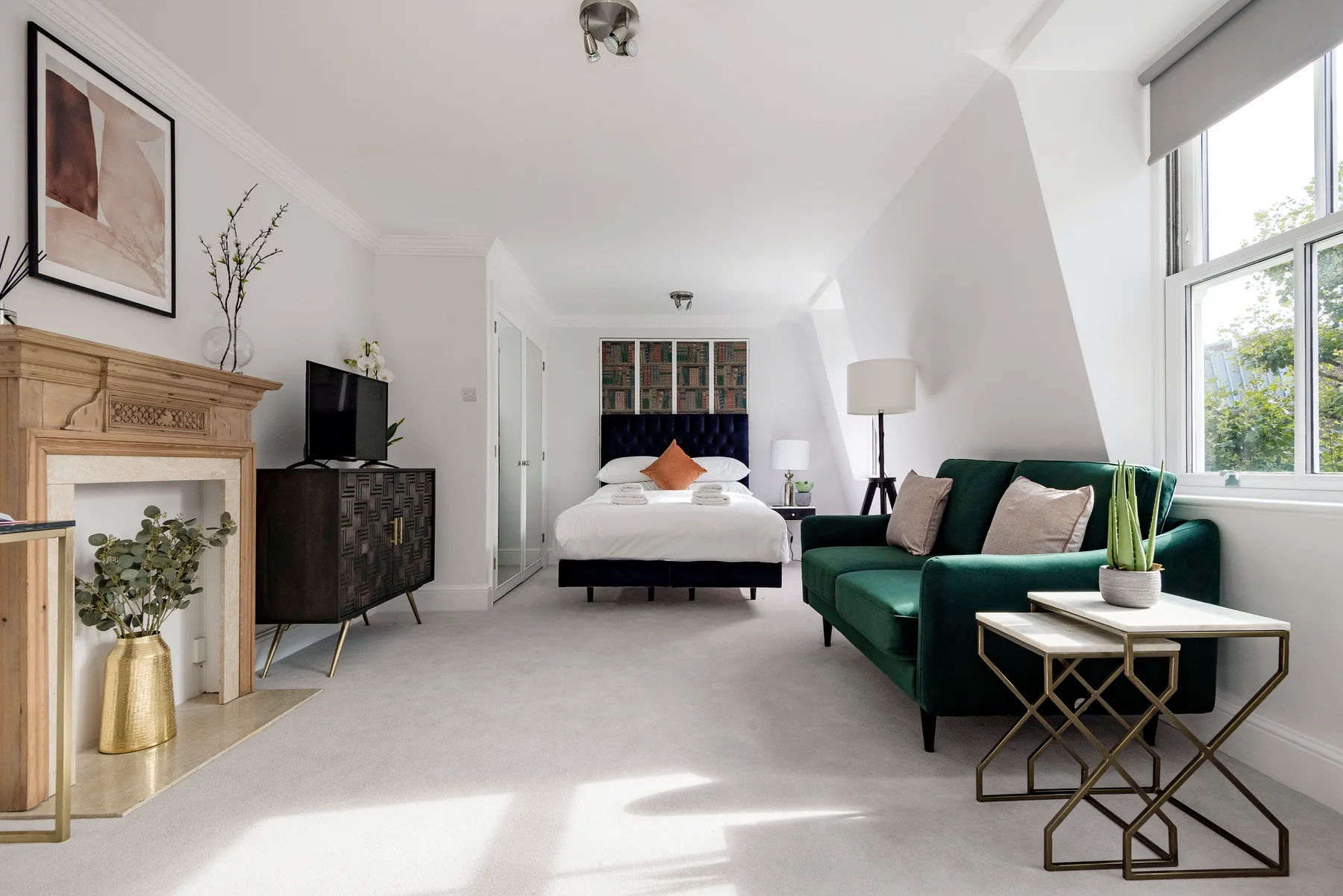 A bright living room with a green seating area and a bed in the background.