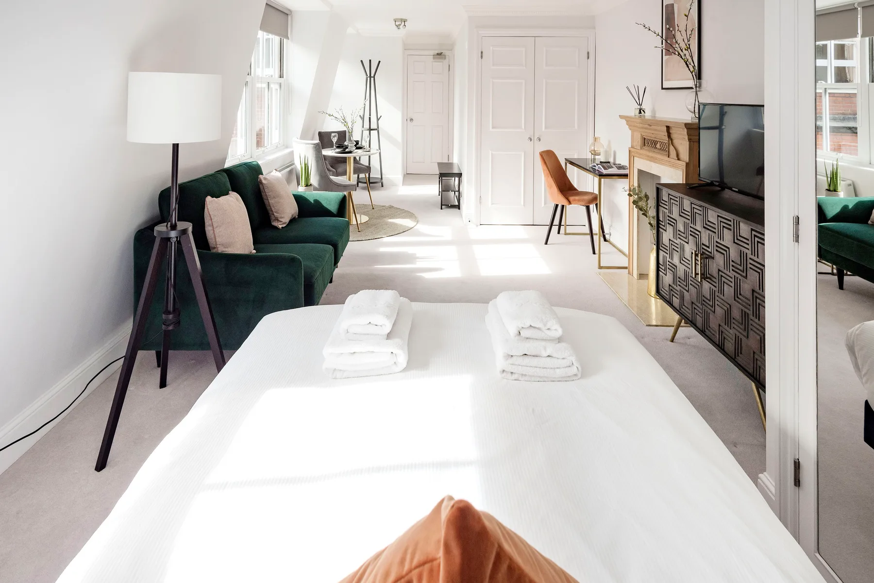 A bright bedroom with a neatly made bed and a dark green seating area.