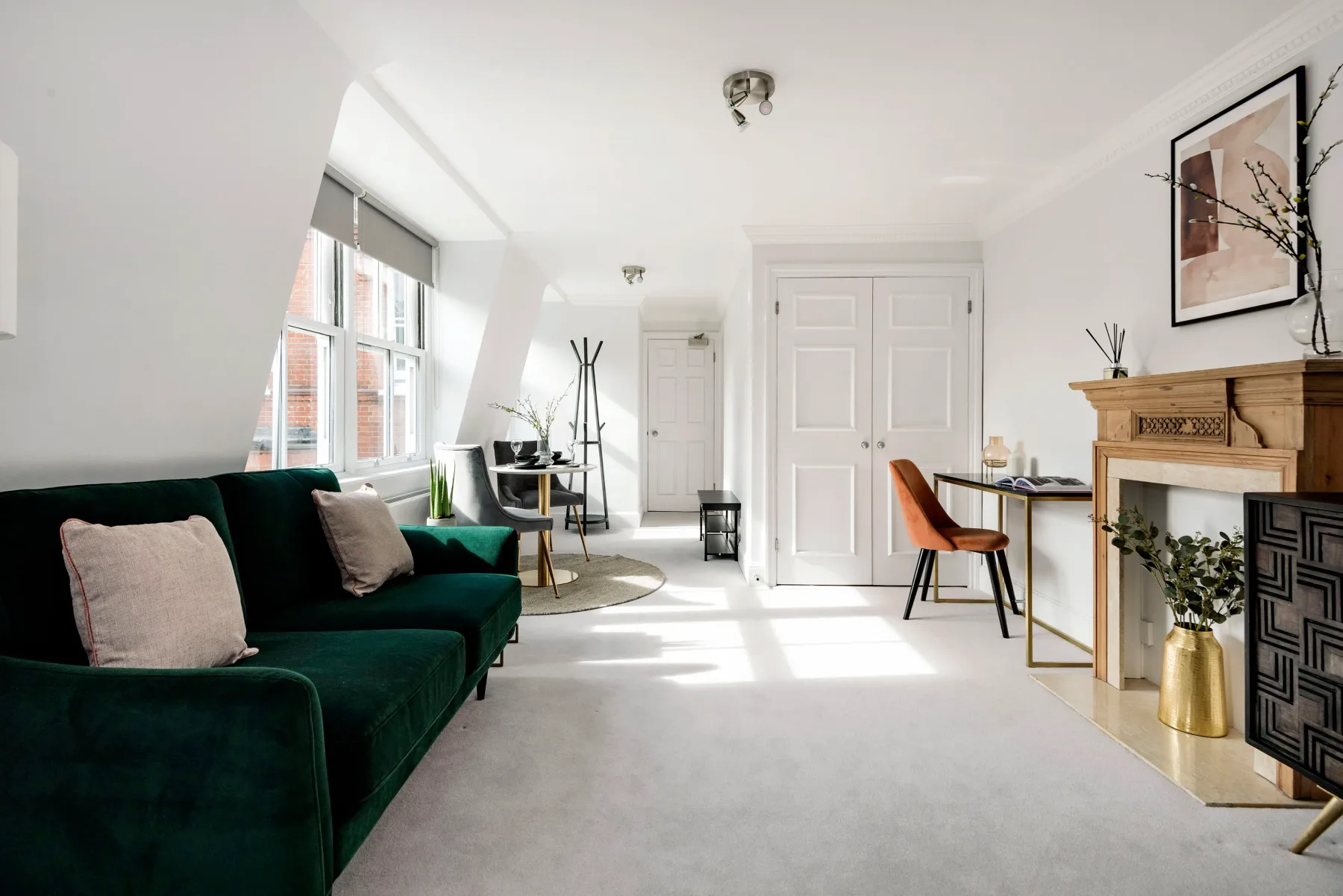 A bright living room with green seating, large windows, and a fireplace.