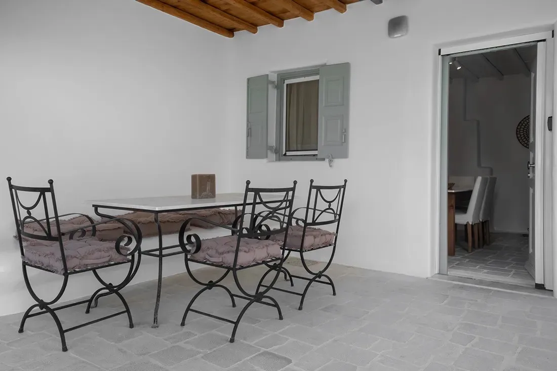 Un comedor con una mesa rectangular y asientos metálicos junto a una puerta abierta.
