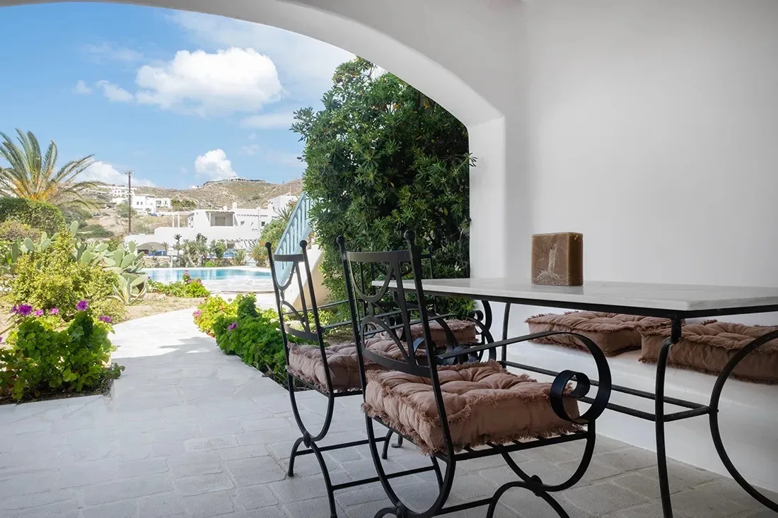 Una zona de estar exterior a la sombra se abre a un sendero ajardinado y una piscina.
