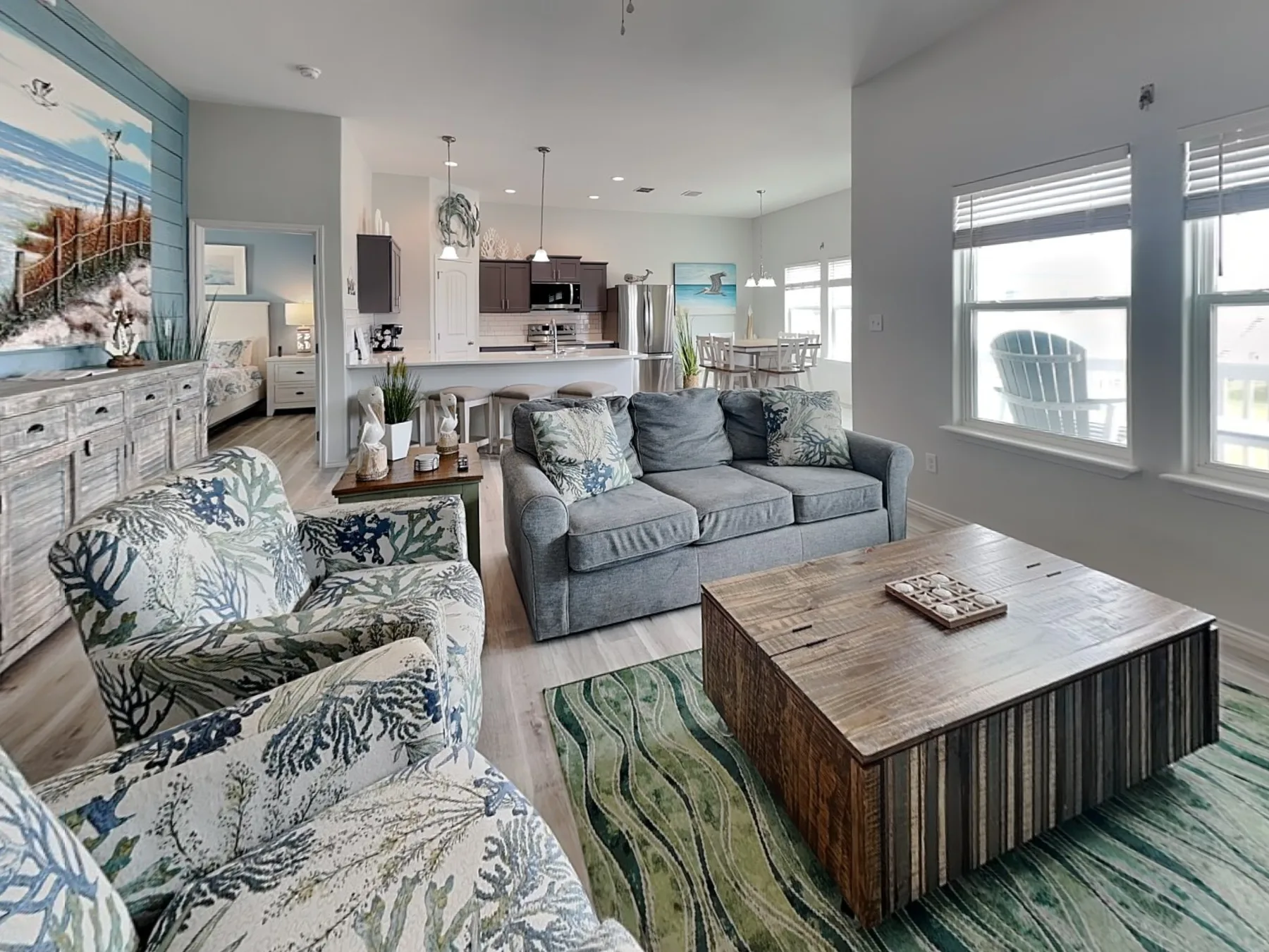 A living room with seating, a coffee table, and an open kitchen beyond.