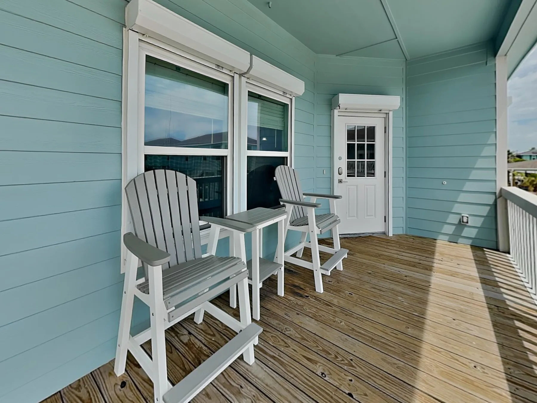 A covered porch with seating beside large windows and a white door.