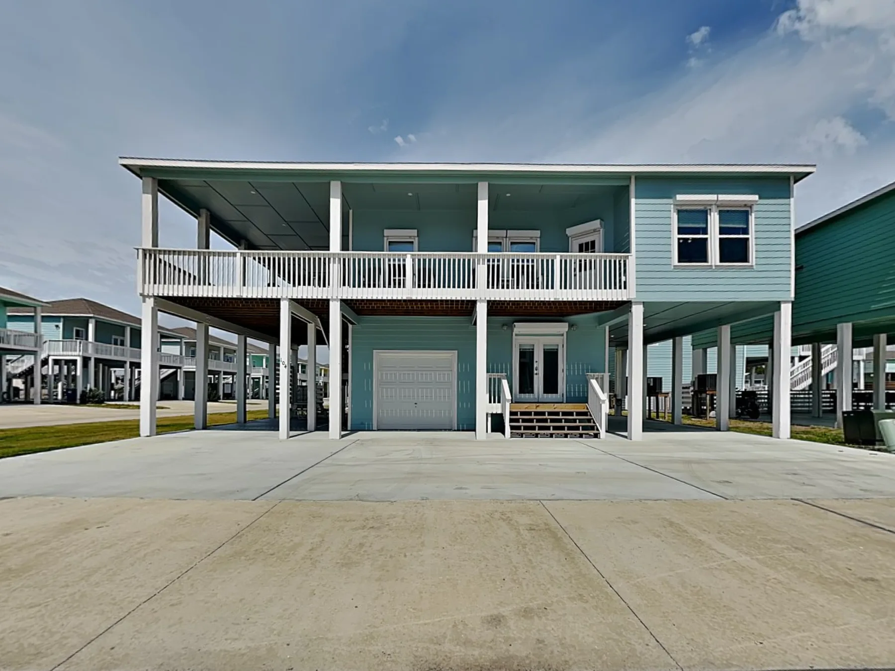 A raised coastal-style house has an open upper balcony and covered parking below.