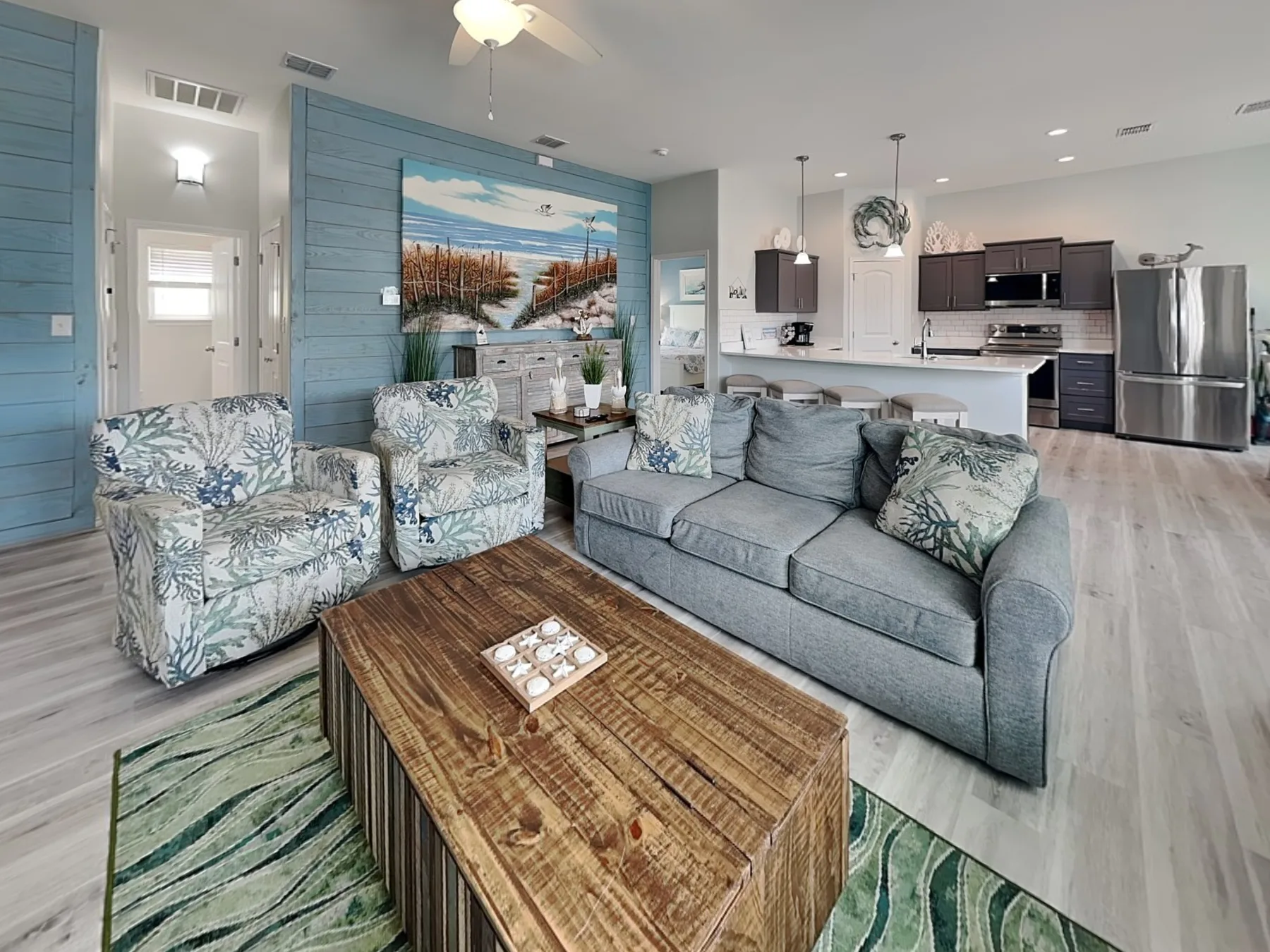 An open-plan living room with a gray sofa and a kitchen behind it.