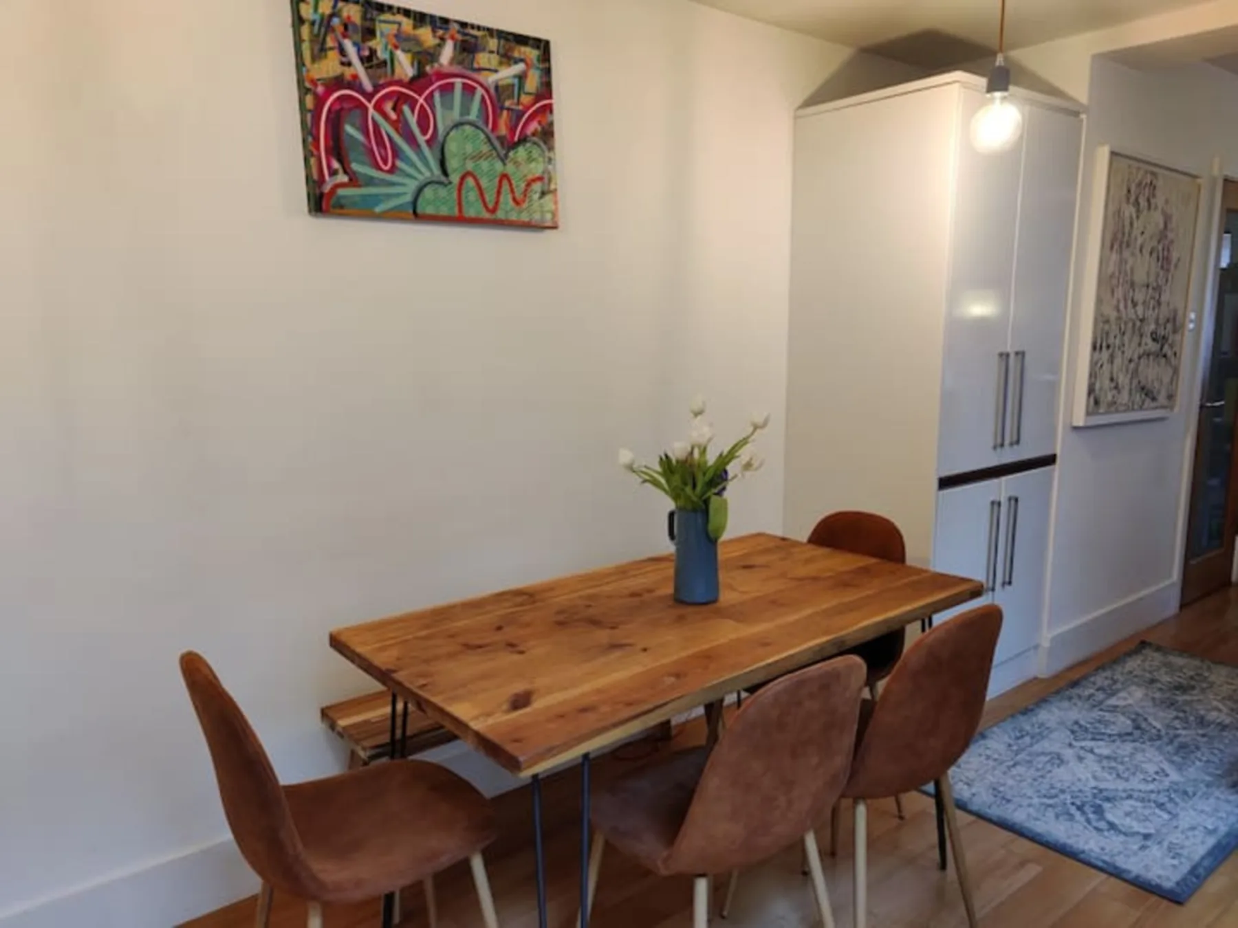 A dining area with a wooden table, chairs, and colorful wall art.
