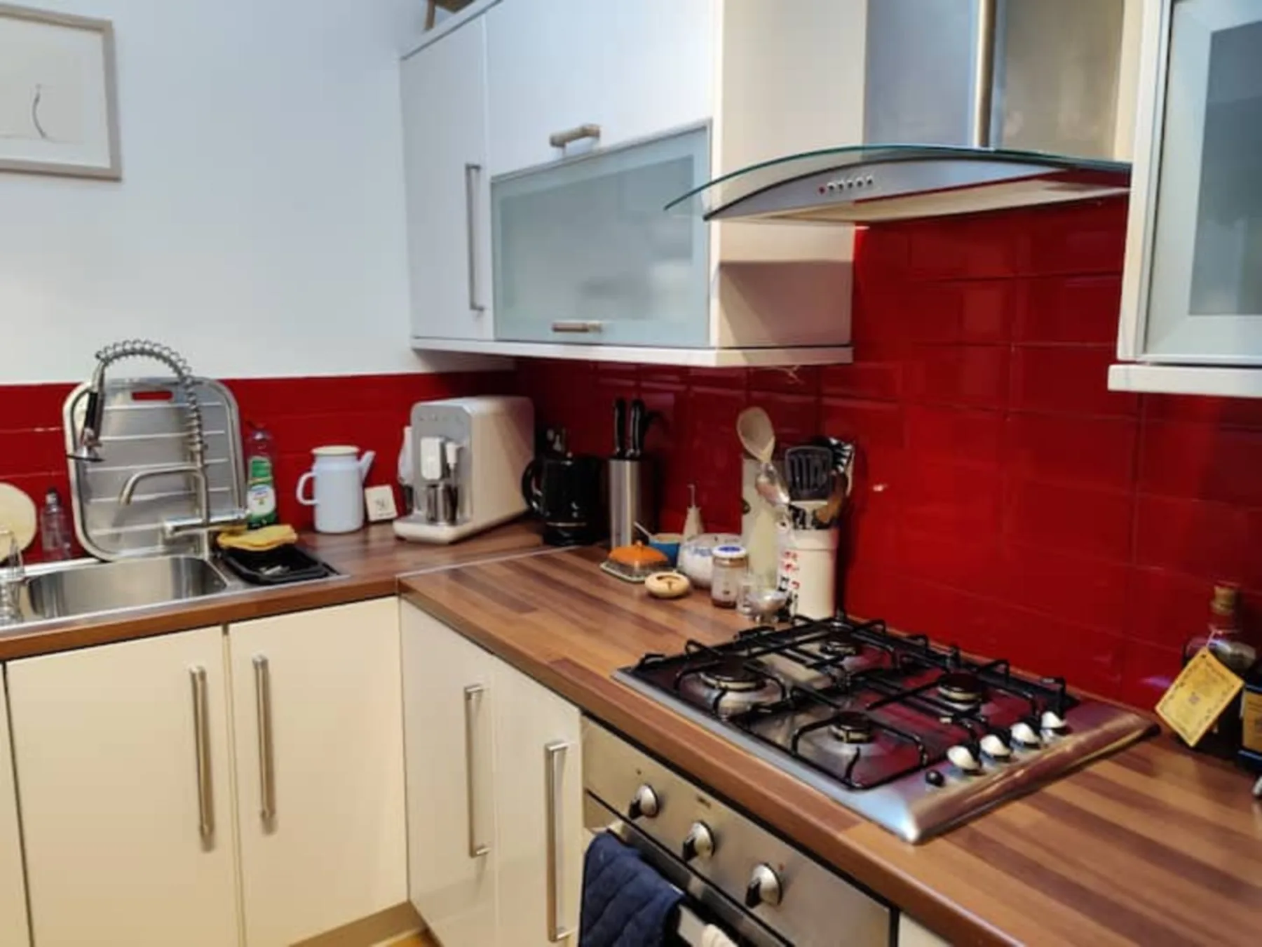 A kitchen with red tile backsplash, countertop, sink, and stovetop.