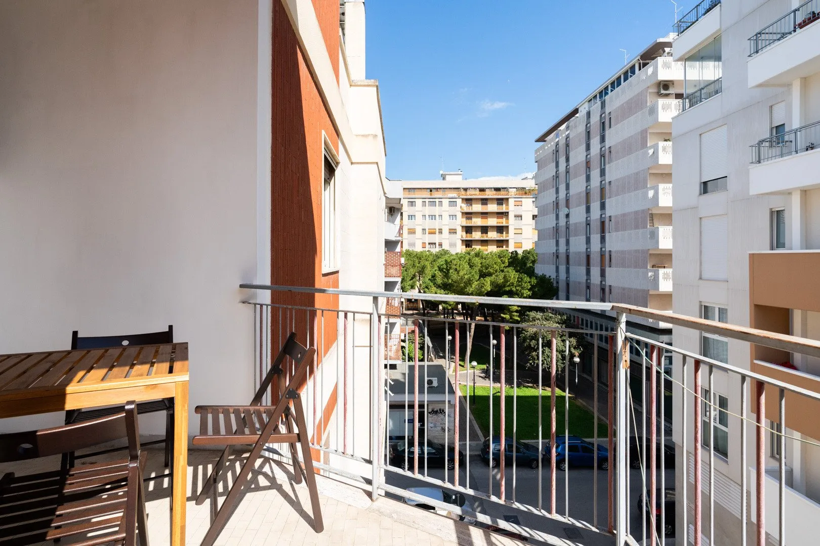 A balcony with outdoor seating overlooks nearby apartment buildings and greenery.