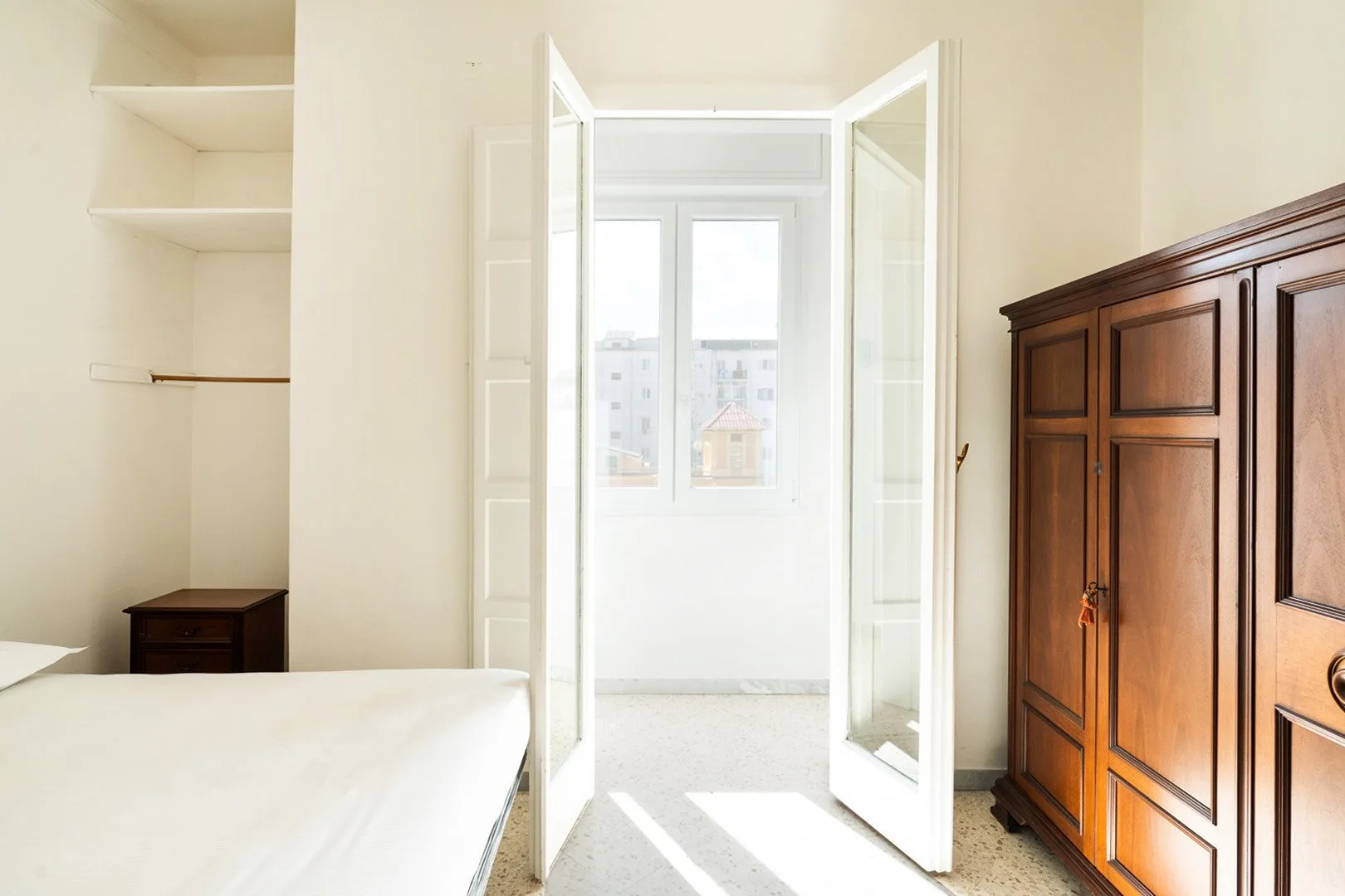 A bright bedroom with a bed, built-in shelves, and open doors to a sunny window.