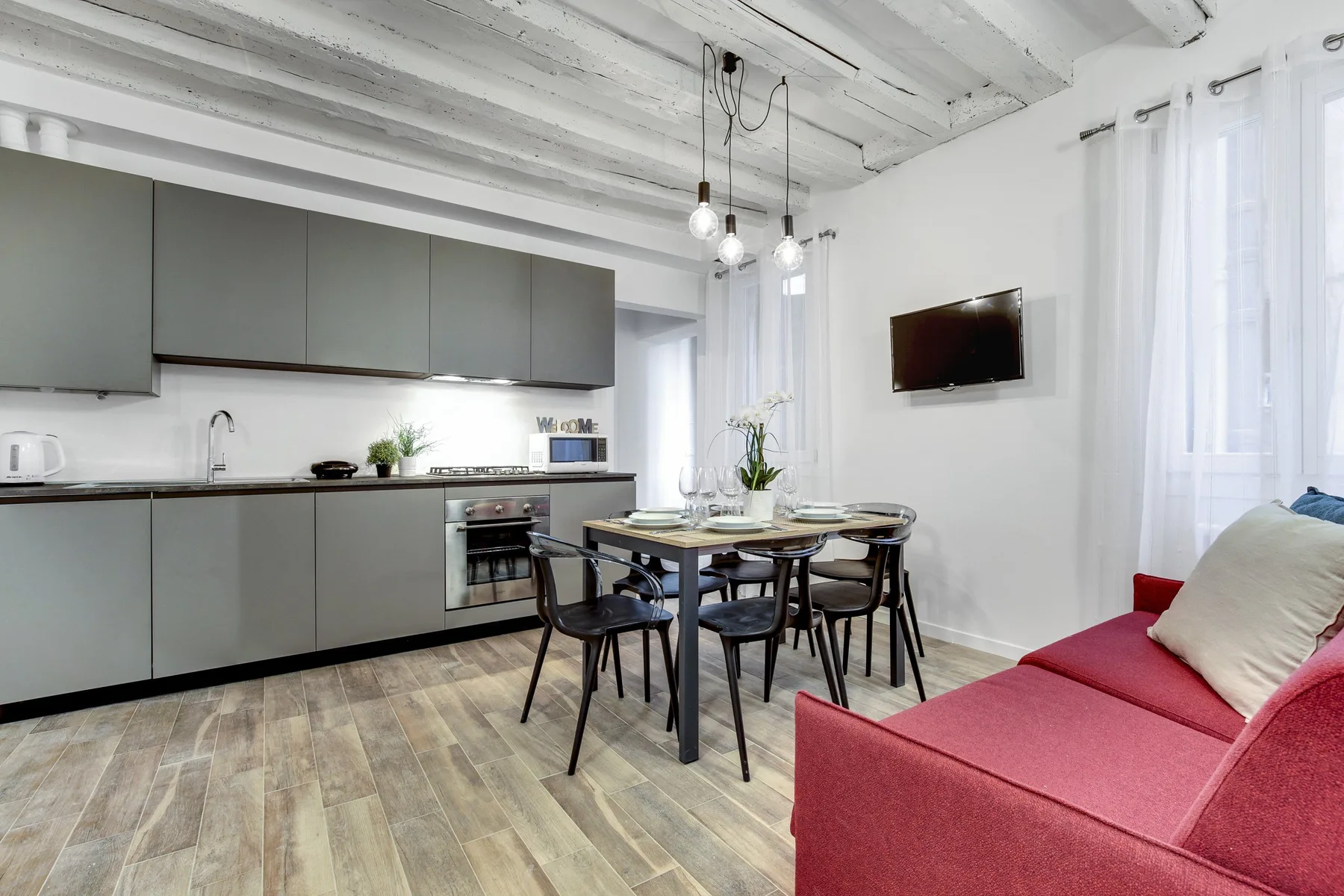 Una luminosa cocina y comedor con un sofá rojo junto a ventanas altas.