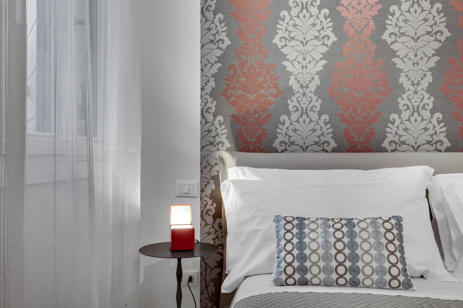 Un dormitorio con una cama junto a una pared estampada y una pequeña mesa de noche.