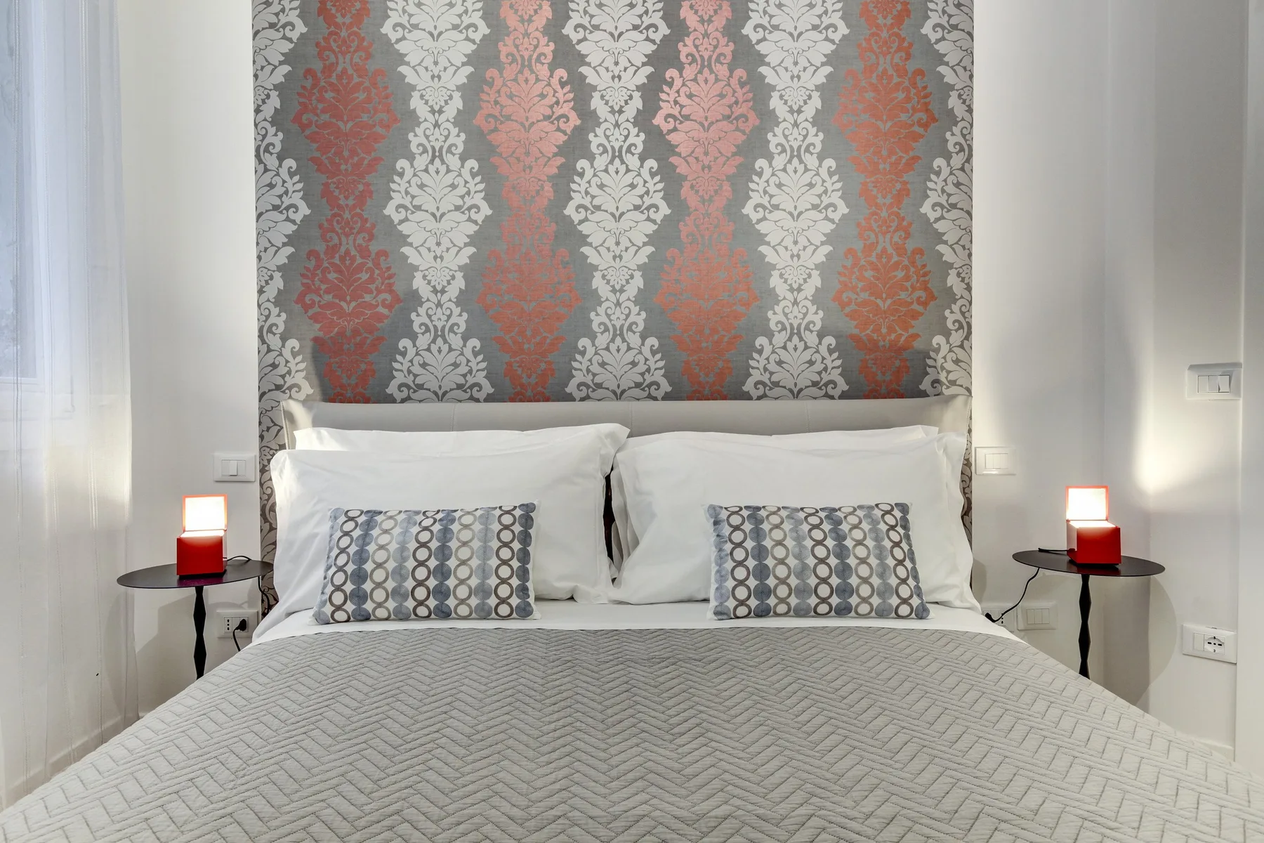 Un dormitorio con una cama bien tendida y papel tapiz estampado detrás del cabecero.