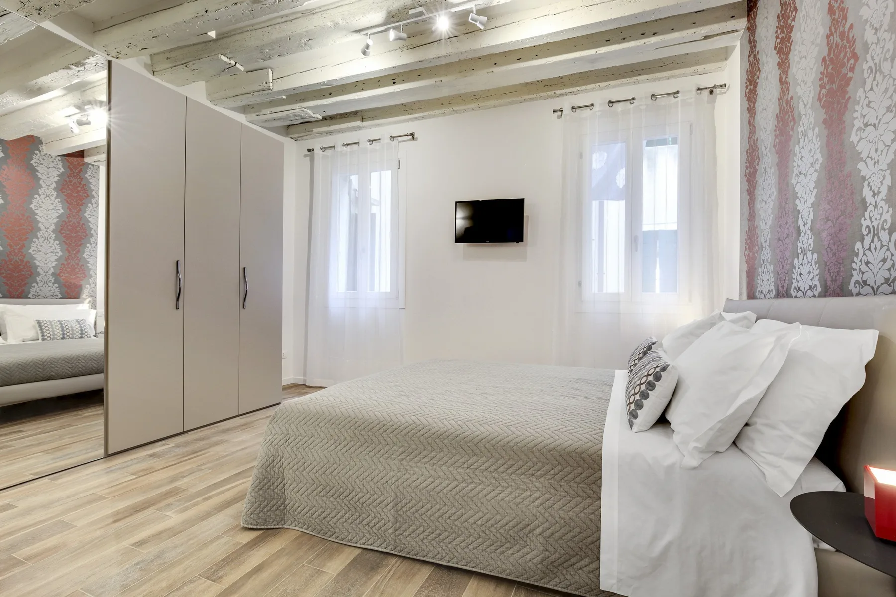Un dormitorio con una cama arreglada, un armario con espejo y un televisor en la pared.