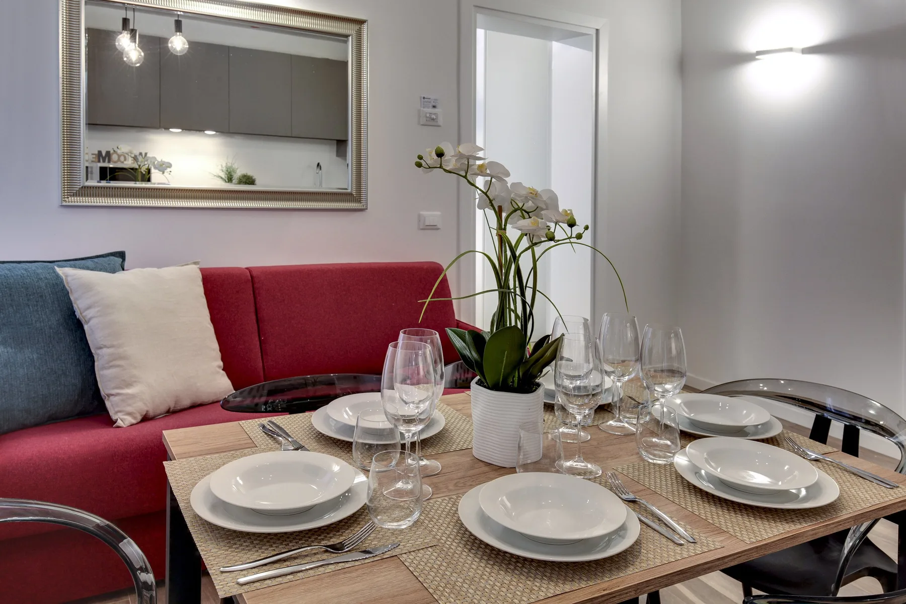 Una mesa de comedor con platos y copas está junto a un sofá colorido.