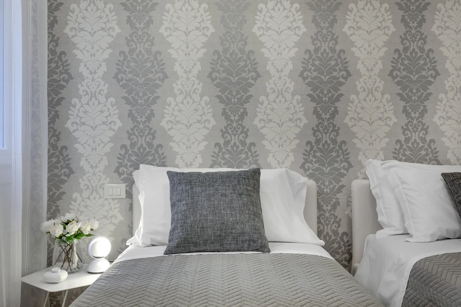 Un dormitorio con dos camas, papel tapiz estampado e iluminación junto a las camas.