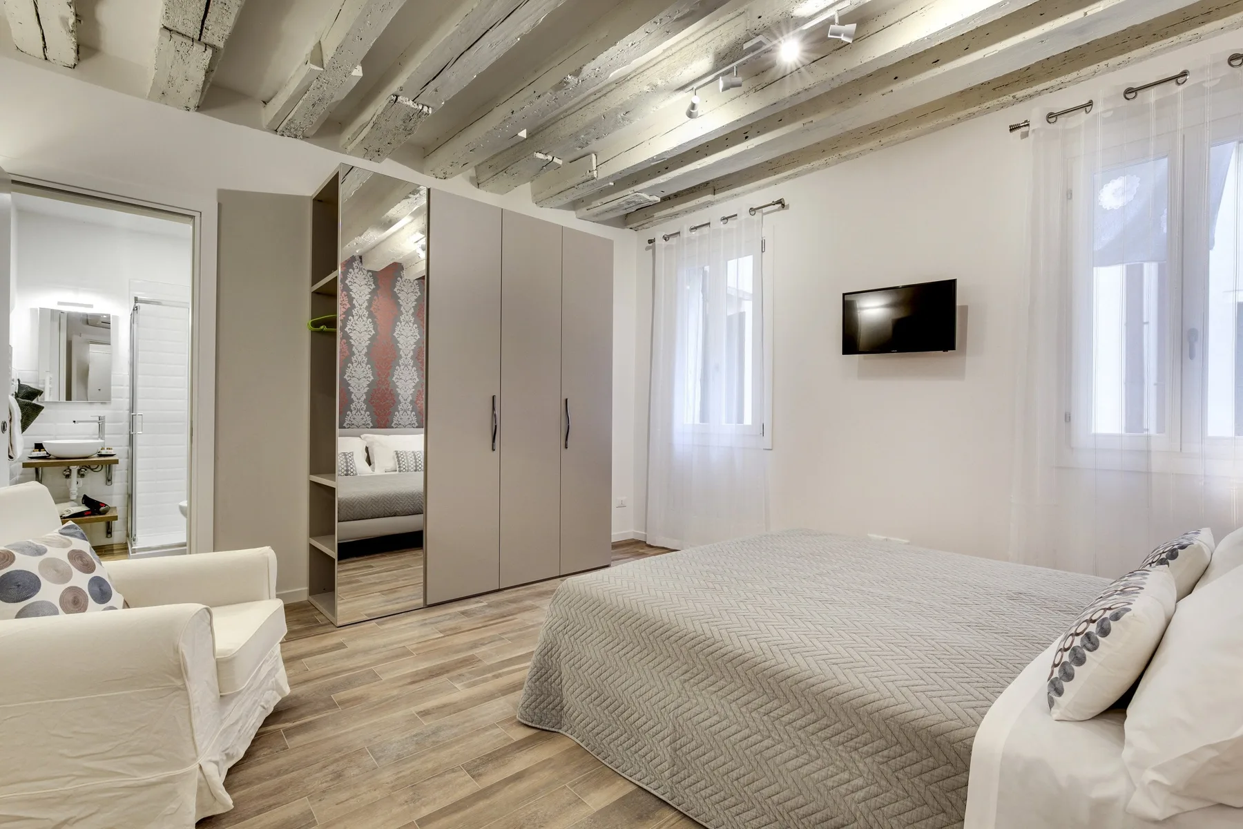 Un dormitorio luminoso con una cama grande, armarios y un televisor en la pared.