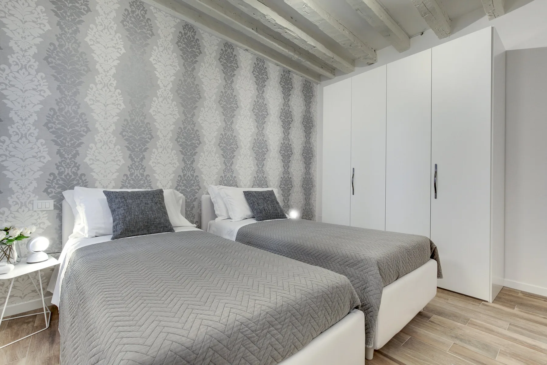 Un dormitorio con dos camas cubiertas de ropa de cama gris y un armario blanco alto.