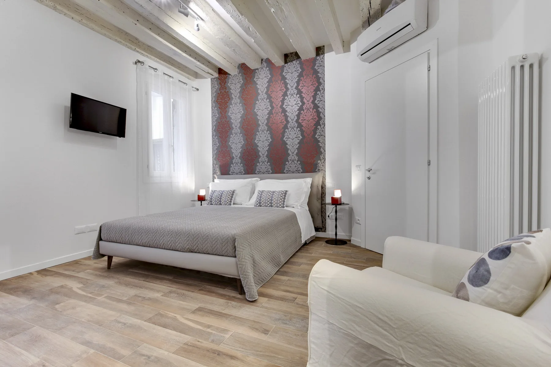 Un dormitorio con una cama, papel tapiz estampado y una zona de asientos blanca.