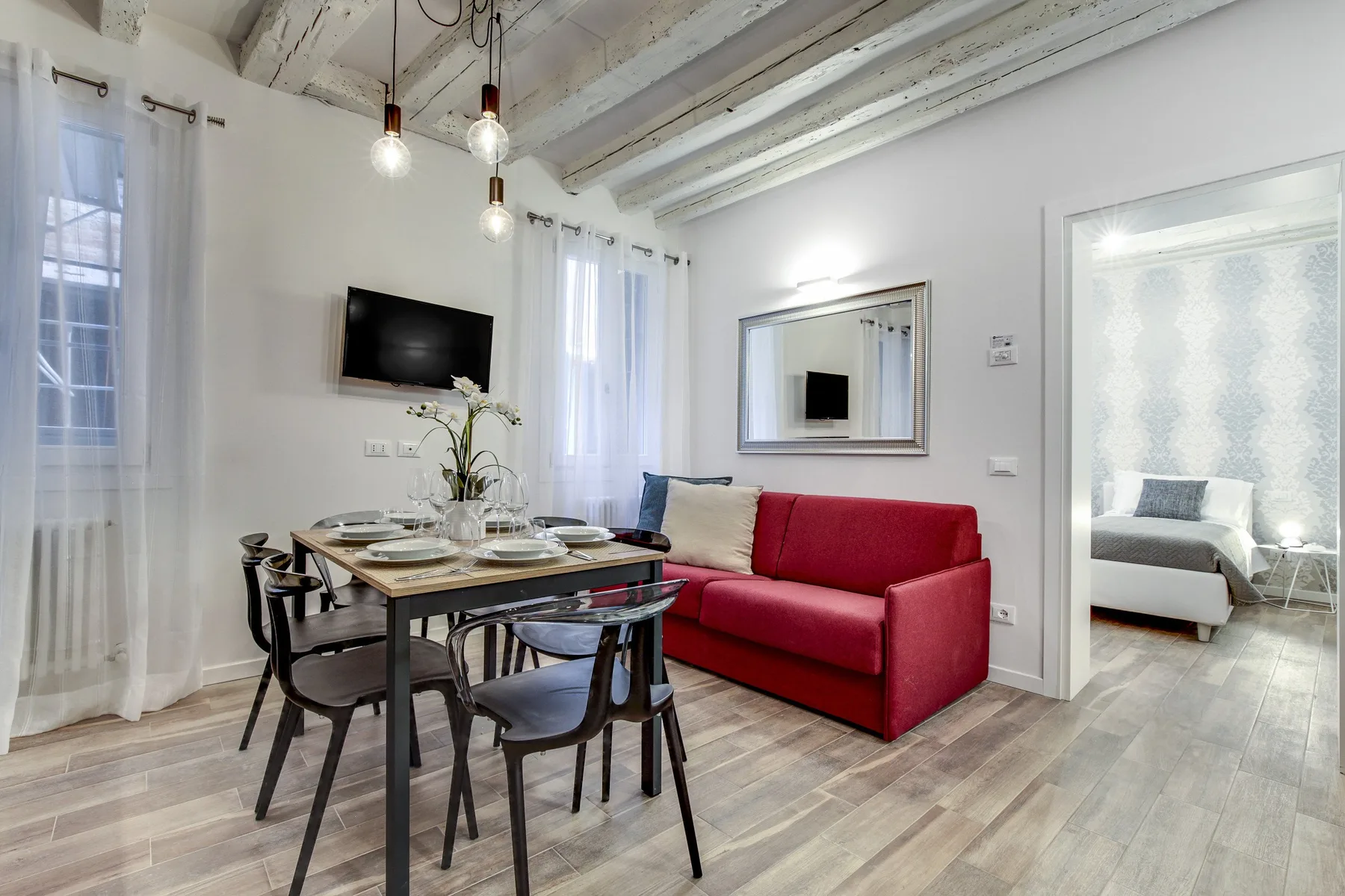 Comedor con mesa y sillas junto a un sofá rojo y un televisor.
