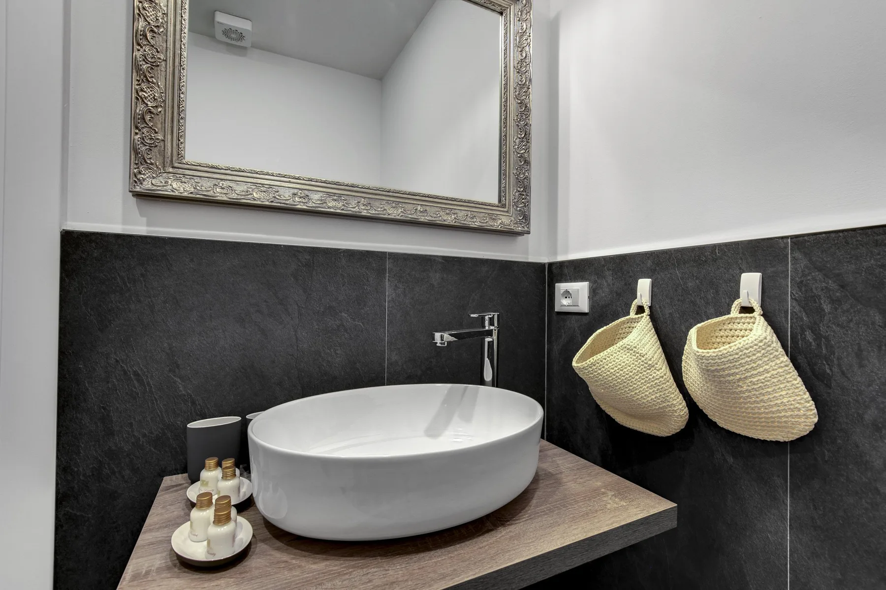 Un lavabo de baño tiene un fregadero blanco sobre una pared de azulejos oscuros.