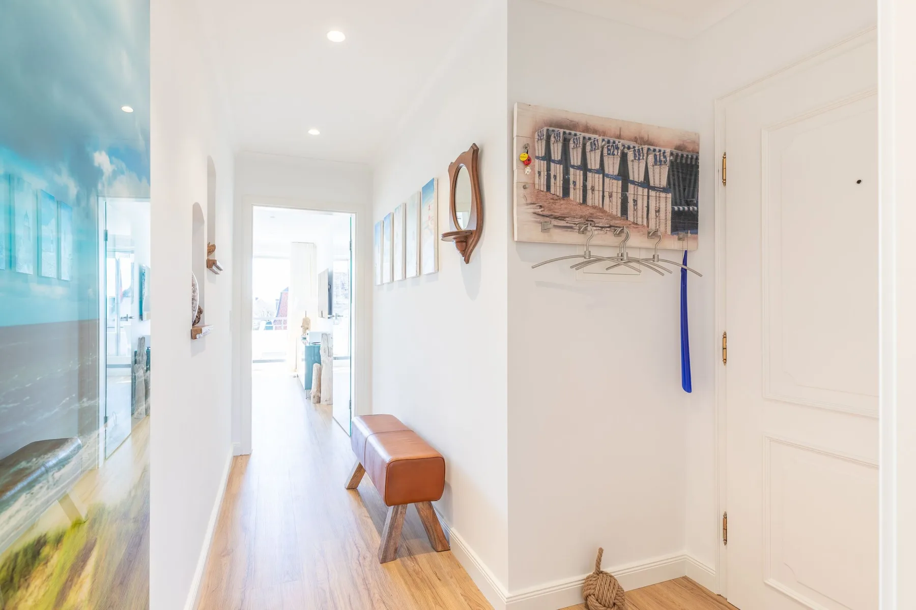 A bright hallway with light wood flooring, wall art, and a small bench.