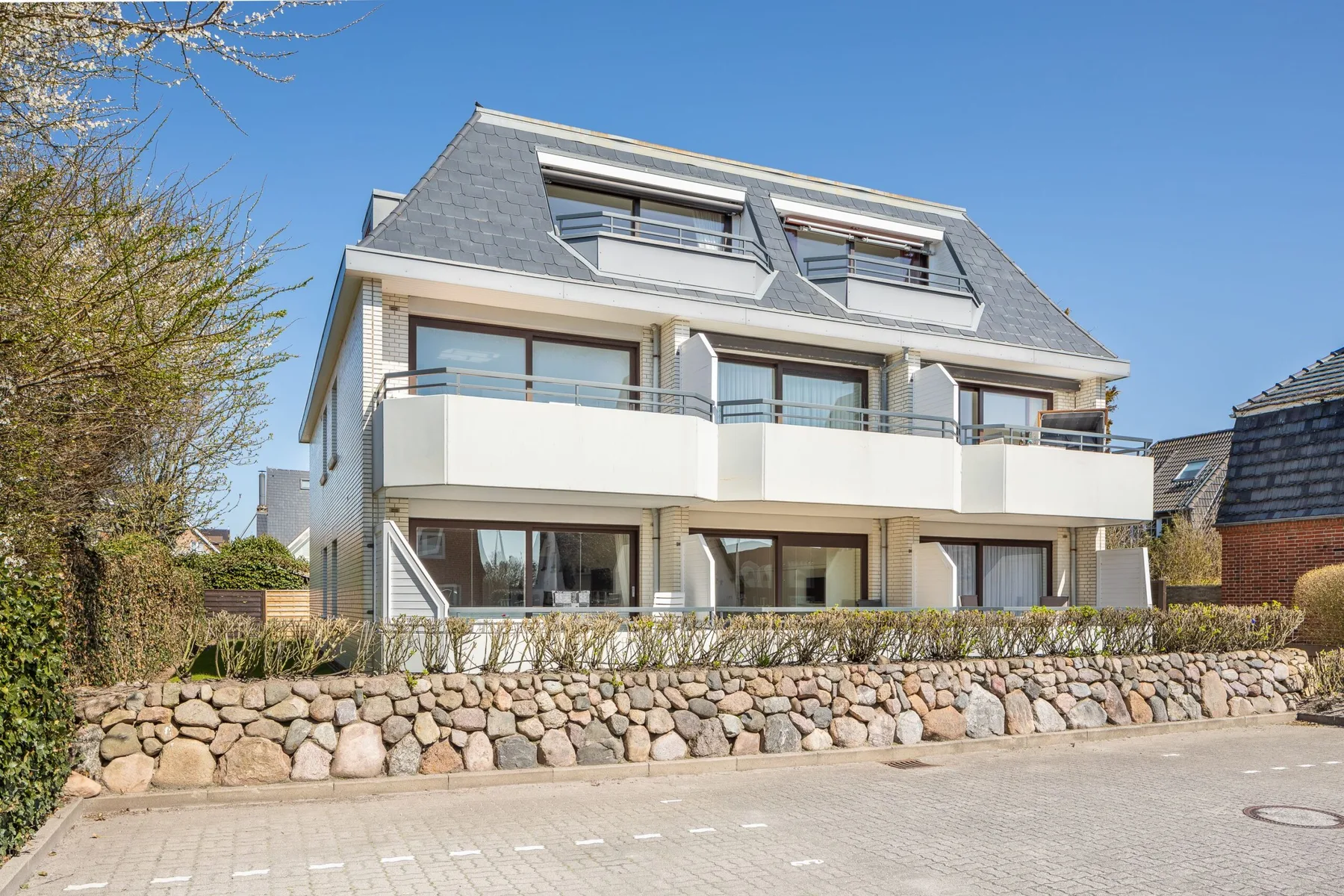 A multi-story residential building with balconies stands behind a low stone wall.