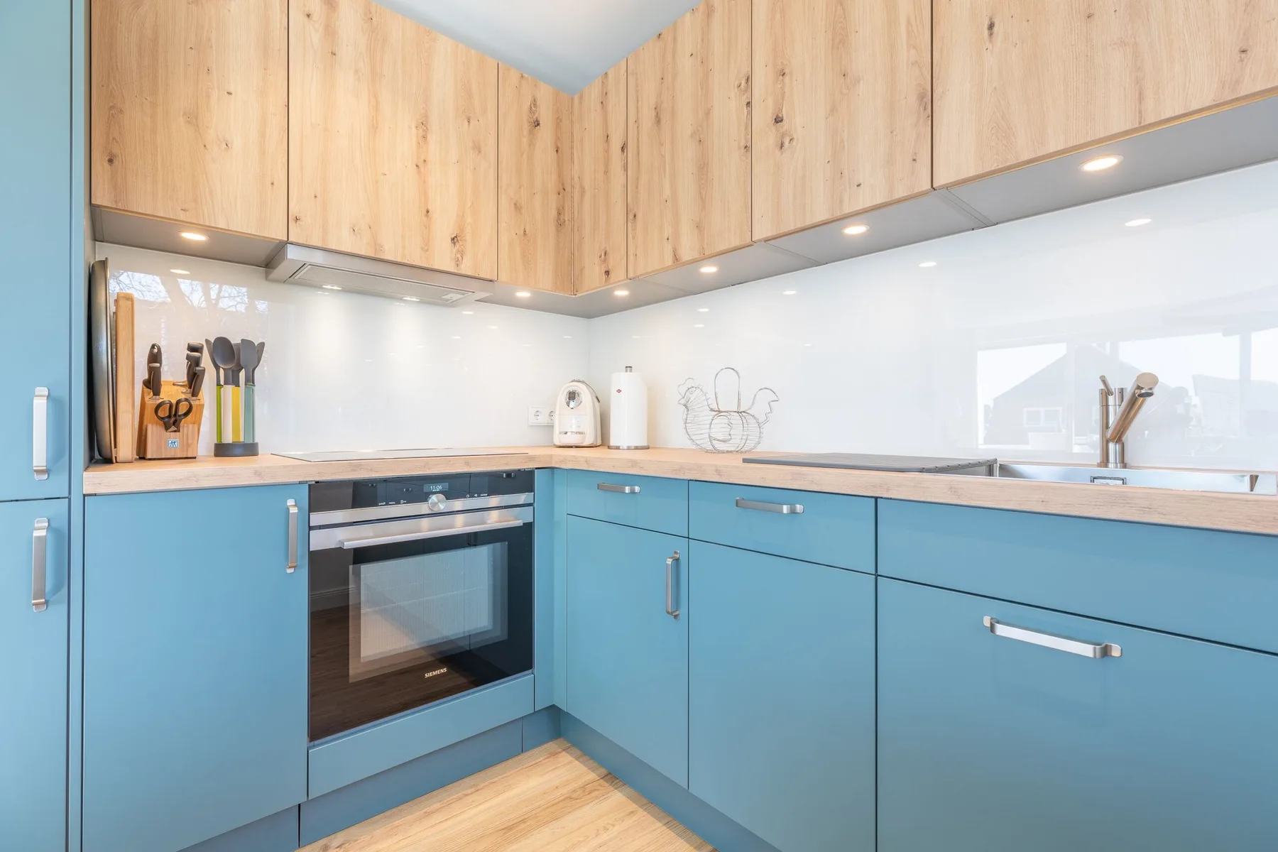 A modern kitchen with blue lower cabinets and light wood upper cabinets.