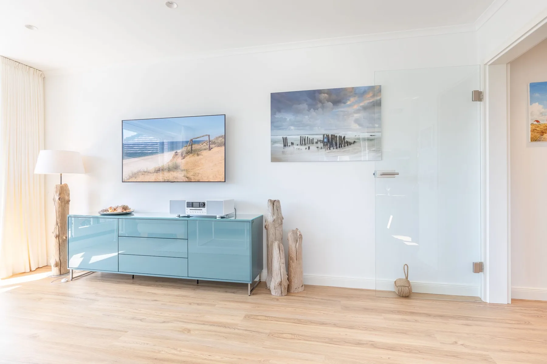 A bright living room features a blue sideboard and two coastal landscape pictures.