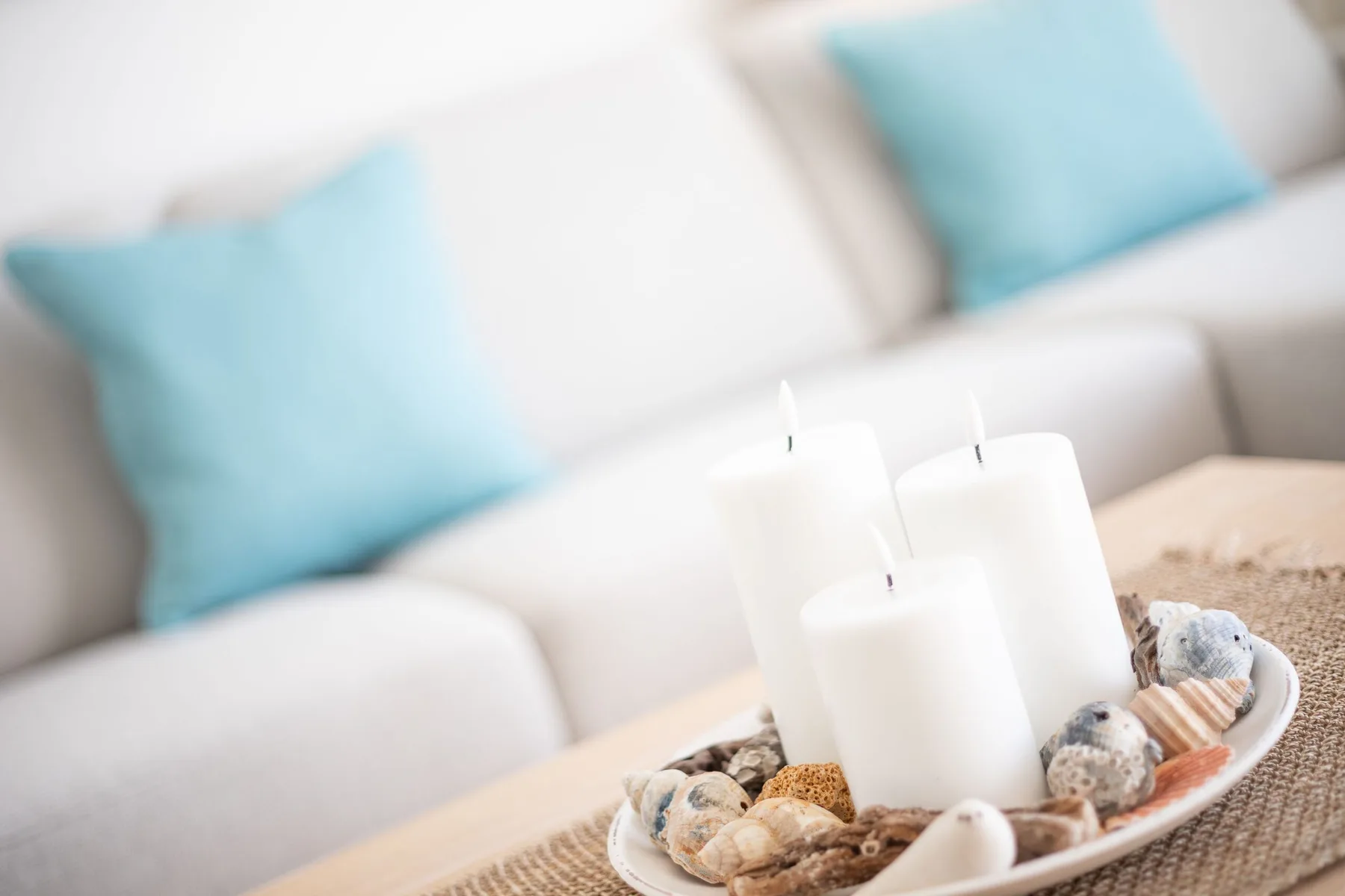 A bright living room with pale seating and a decorative tray of candles and shells.