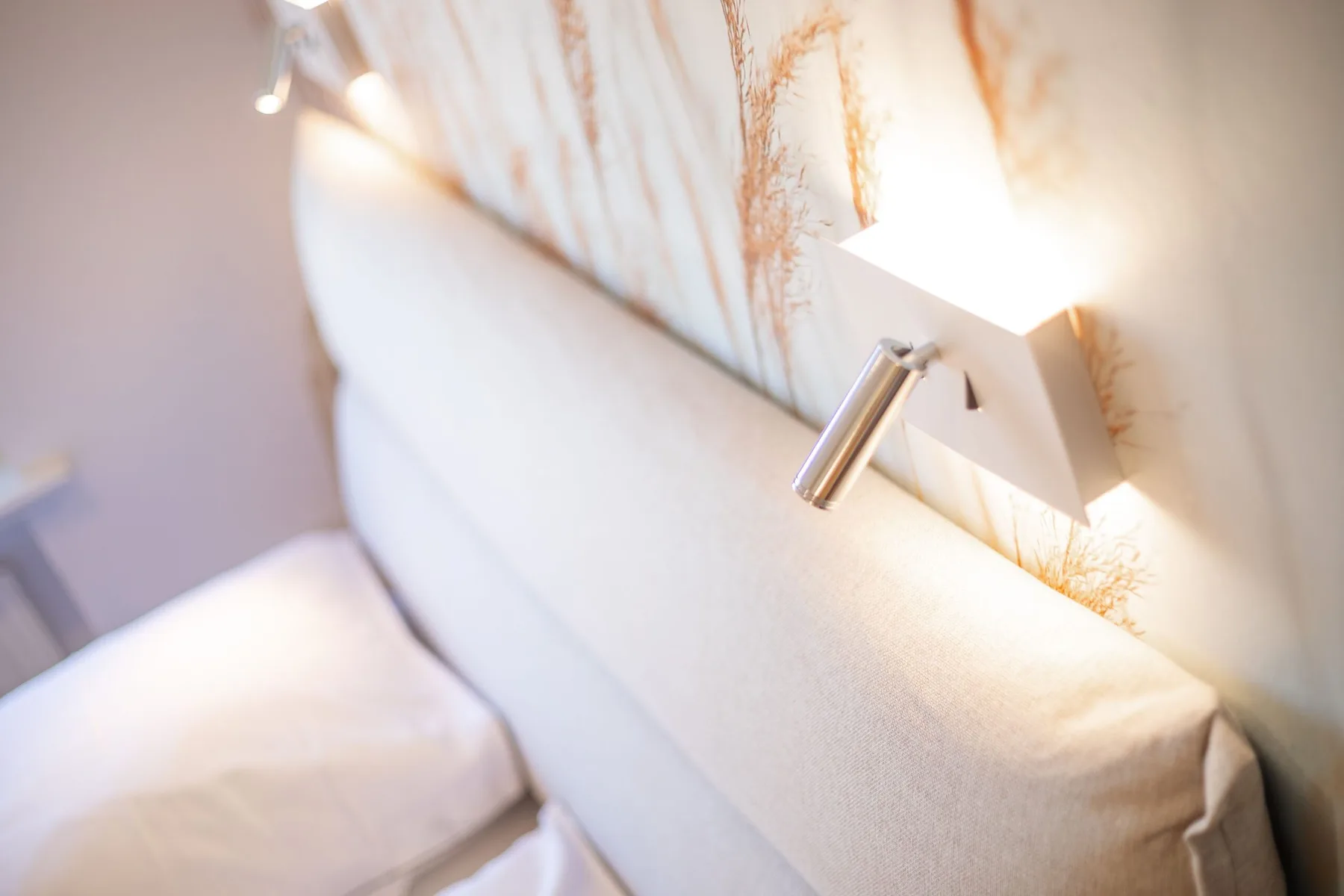 A bedroom scene with a padded headboard and a wall-mounted reading light.