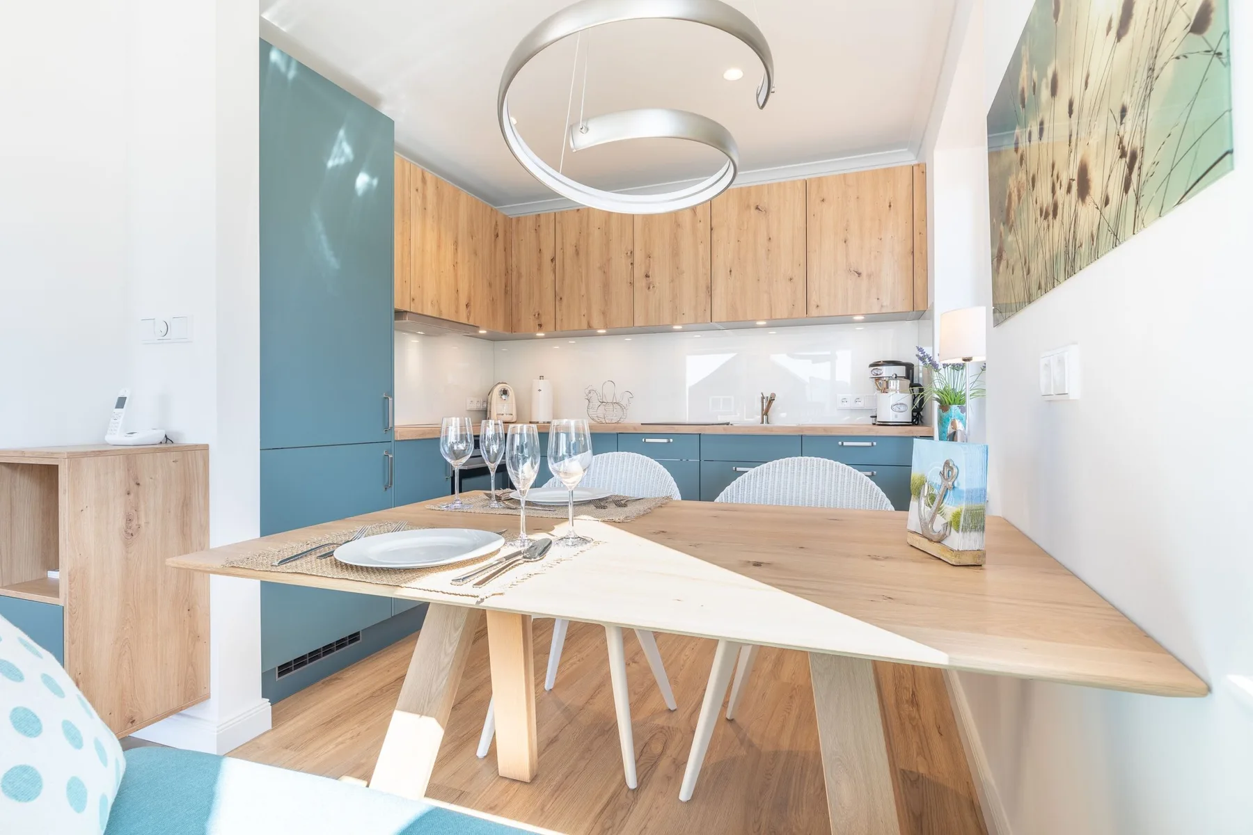A bright dining area with a wooden table set in front of a compact kitchen.