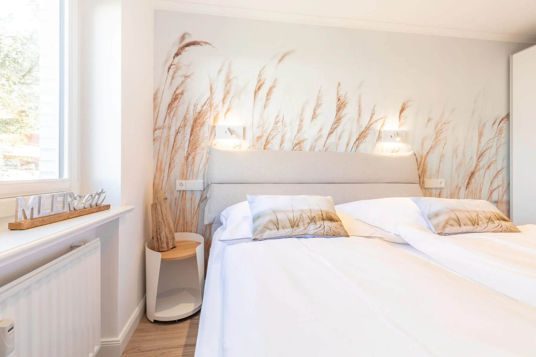 A bright bedroom with a neatly made bed and botanical wall mural.
