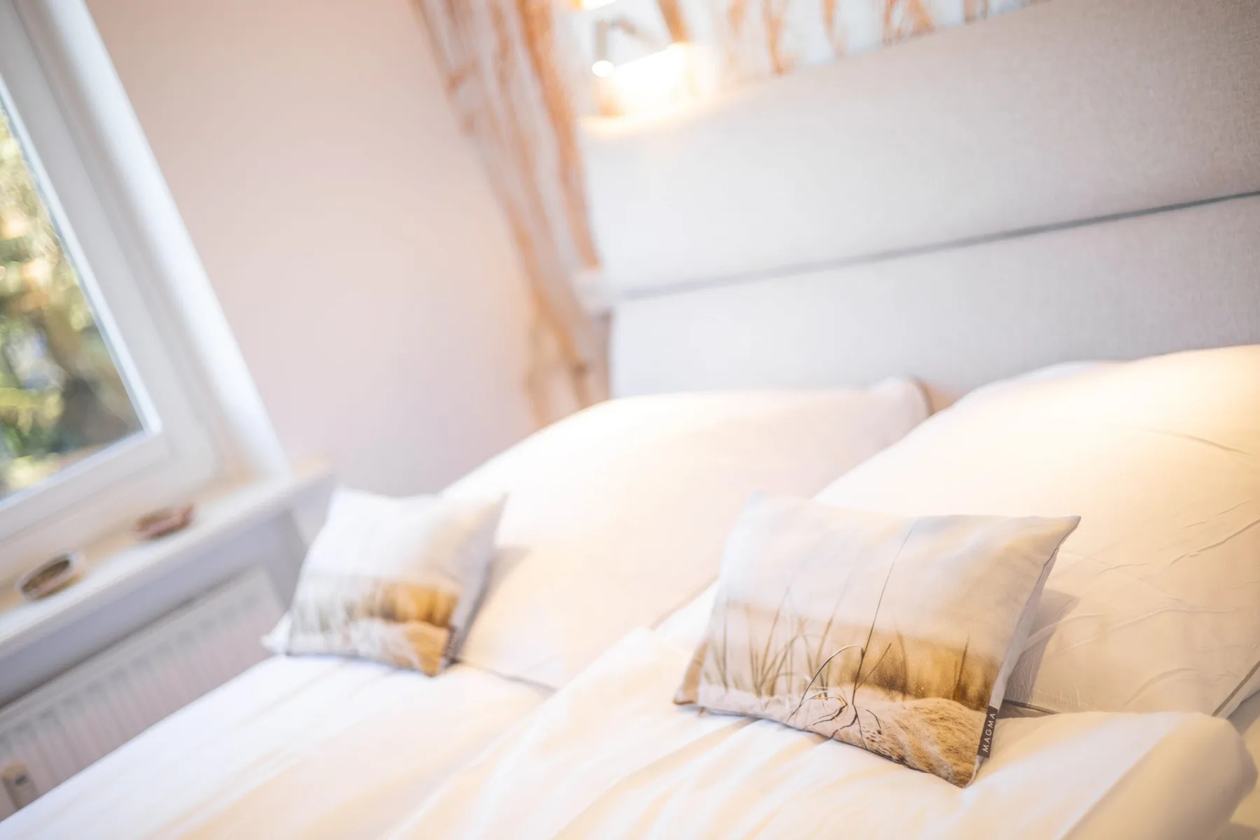 A bright bedroom with white bedding and decorative pillows.