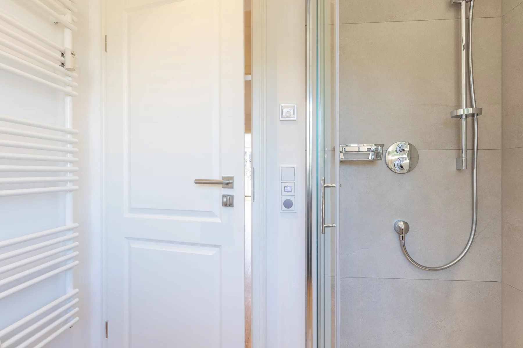 A bathroom shower with a white door and wall-mounted towel warmer.