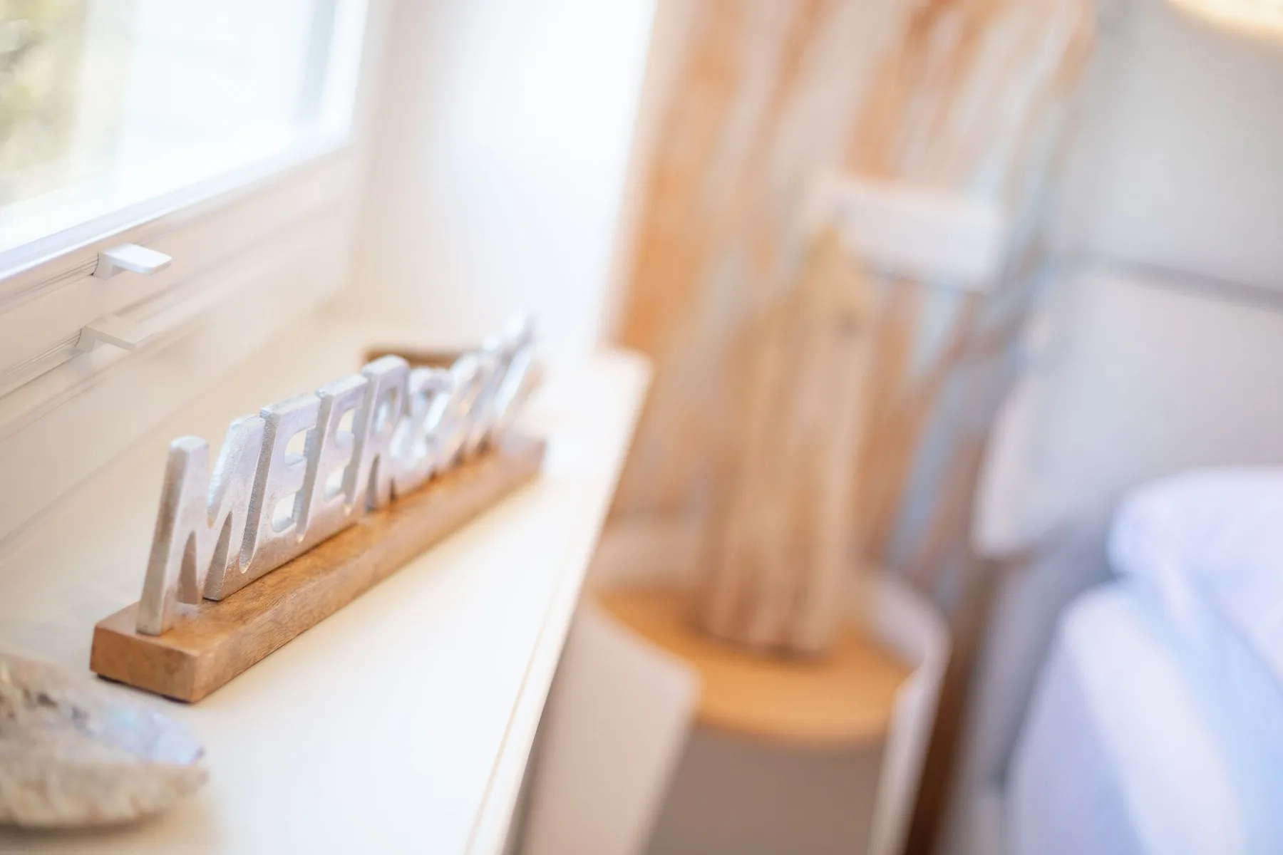 A bright bedroom with a decorative word sign on the windowsill beside the bed.