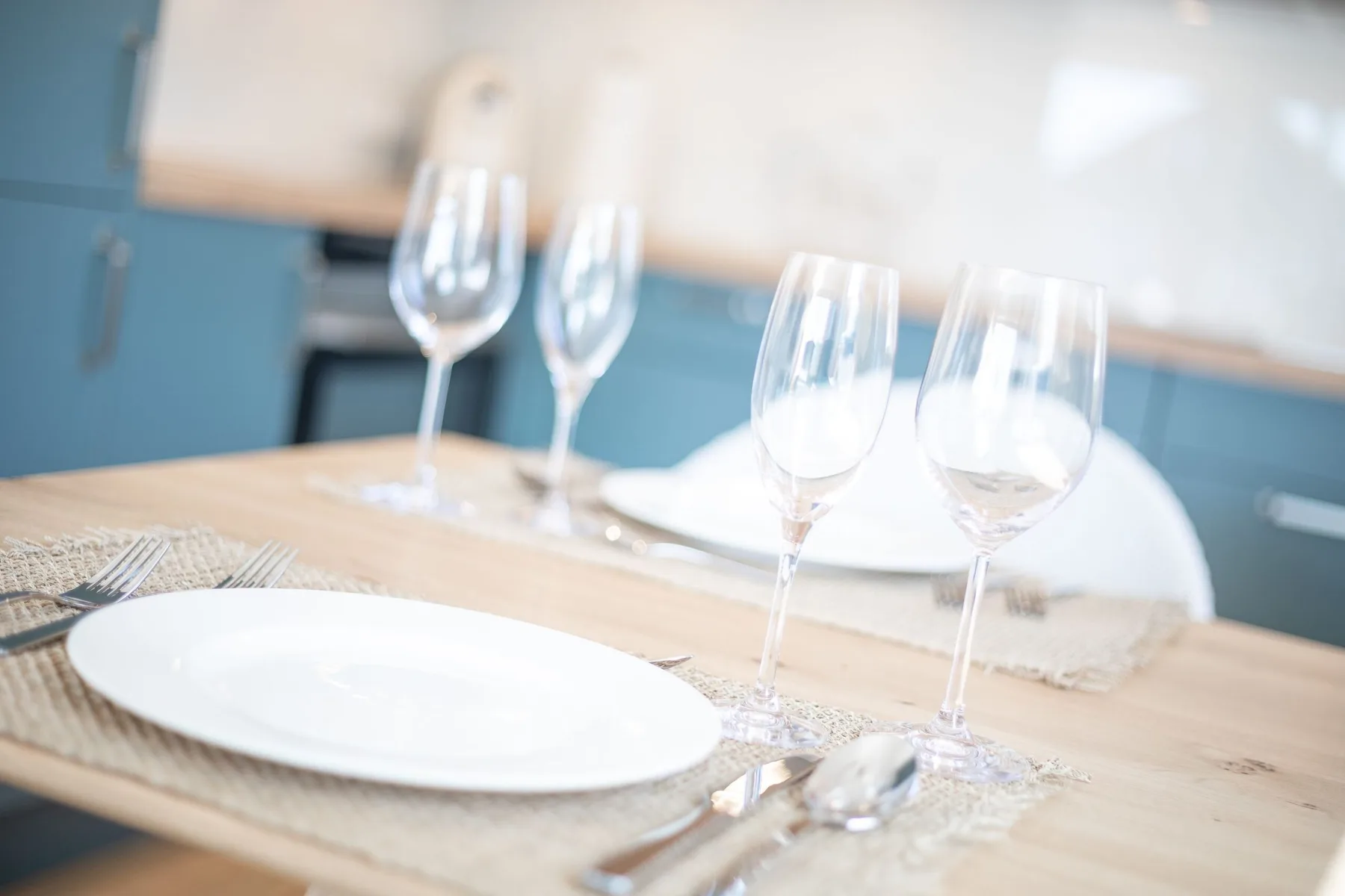 A dining table is set with plates and wine glasses in a bright kitchen.