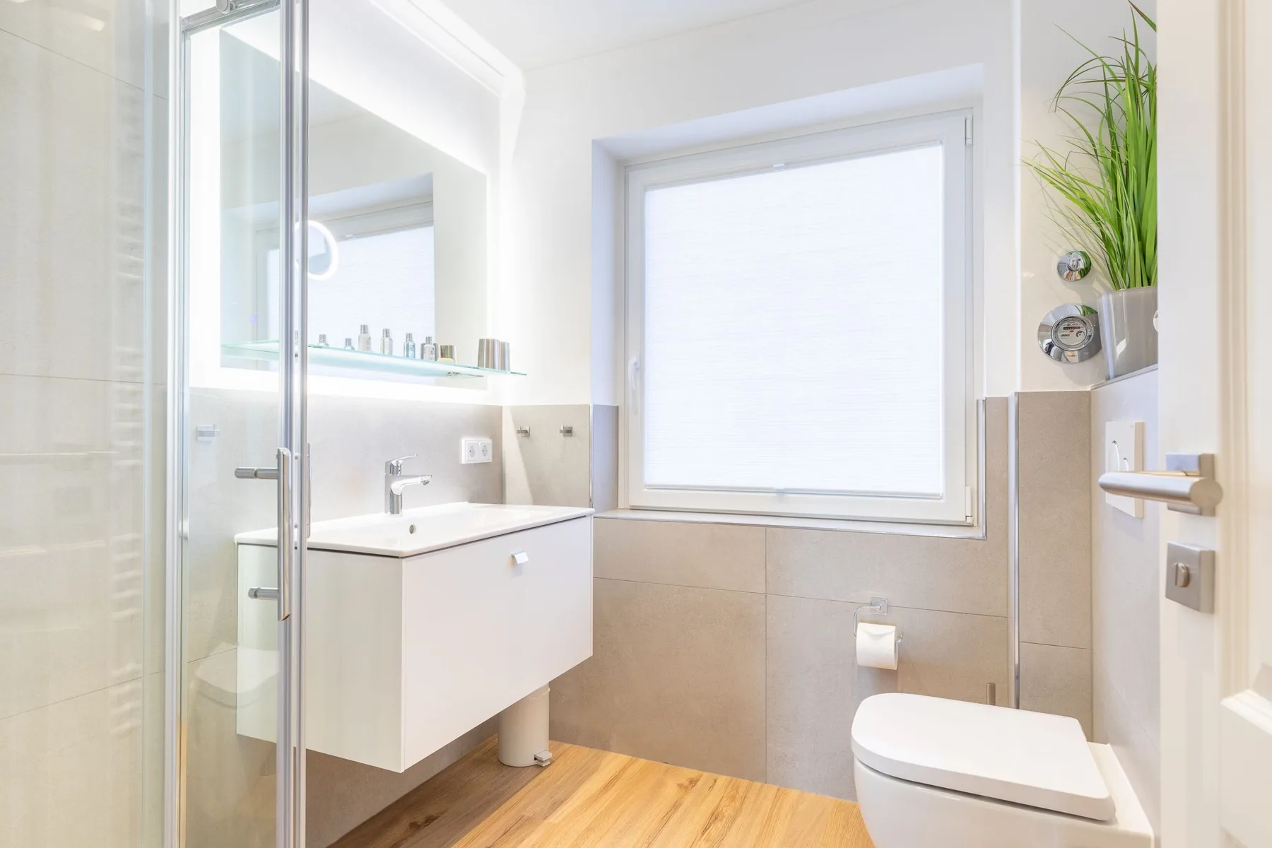 A bright bathroom with a glass shower, sink, and toilet.