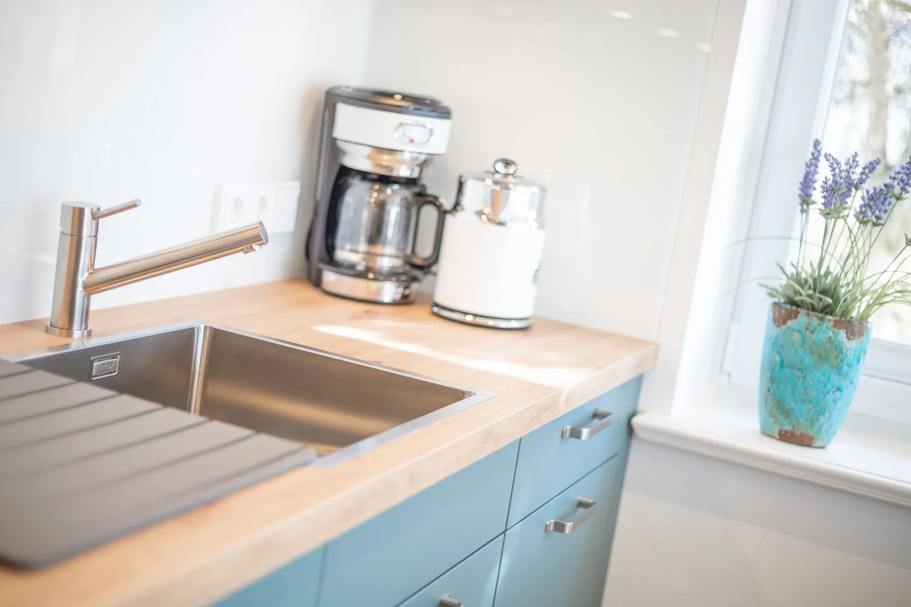 A kitchen counter with a sink, coffee maker, and potted flowers by the window.