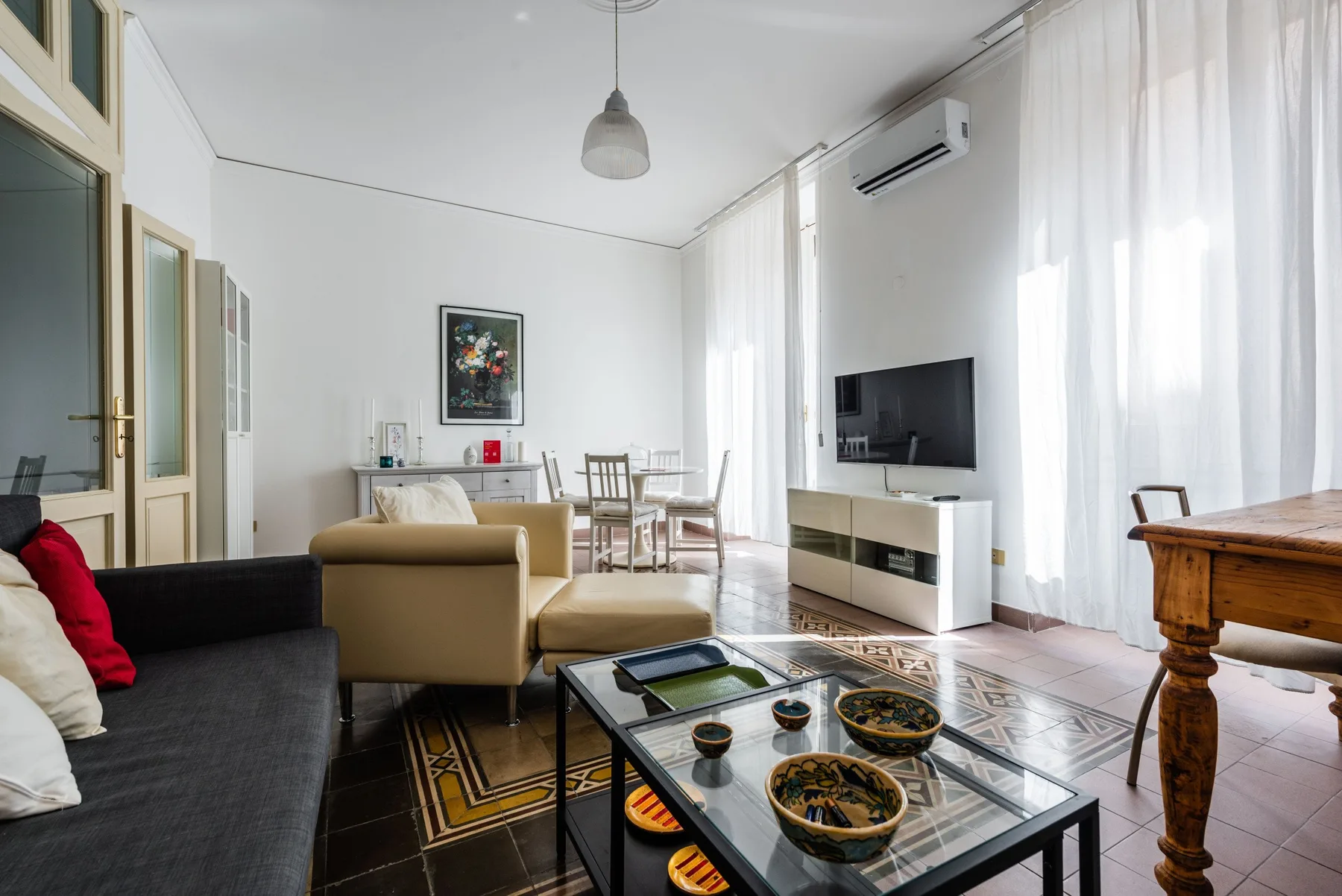 A bright living room with seating, a glass coffee table, and a television.