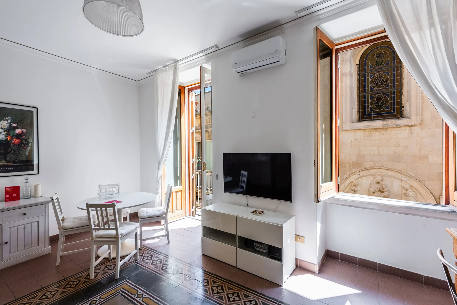 A bright living and dining room with a television and open windows.