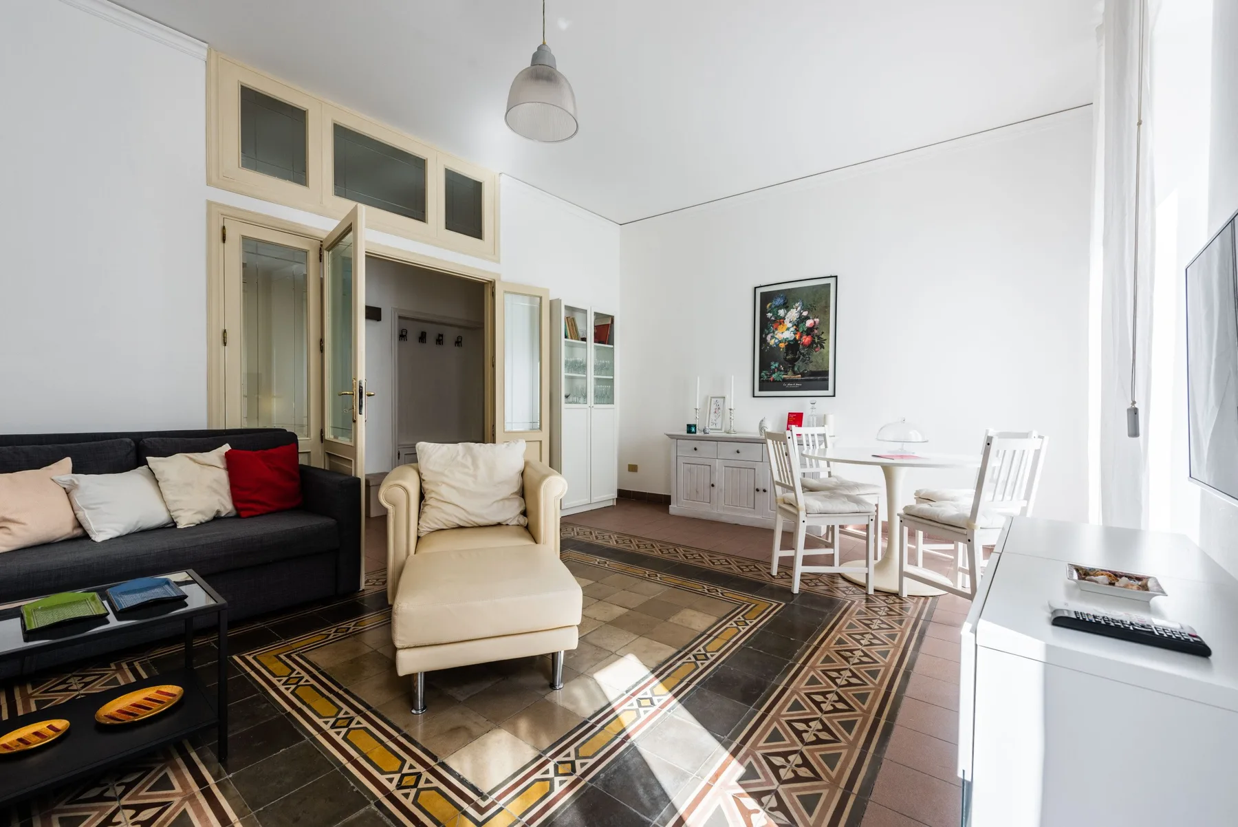 A bright living and dining room with seating, a table, and patterned floor tiles.
