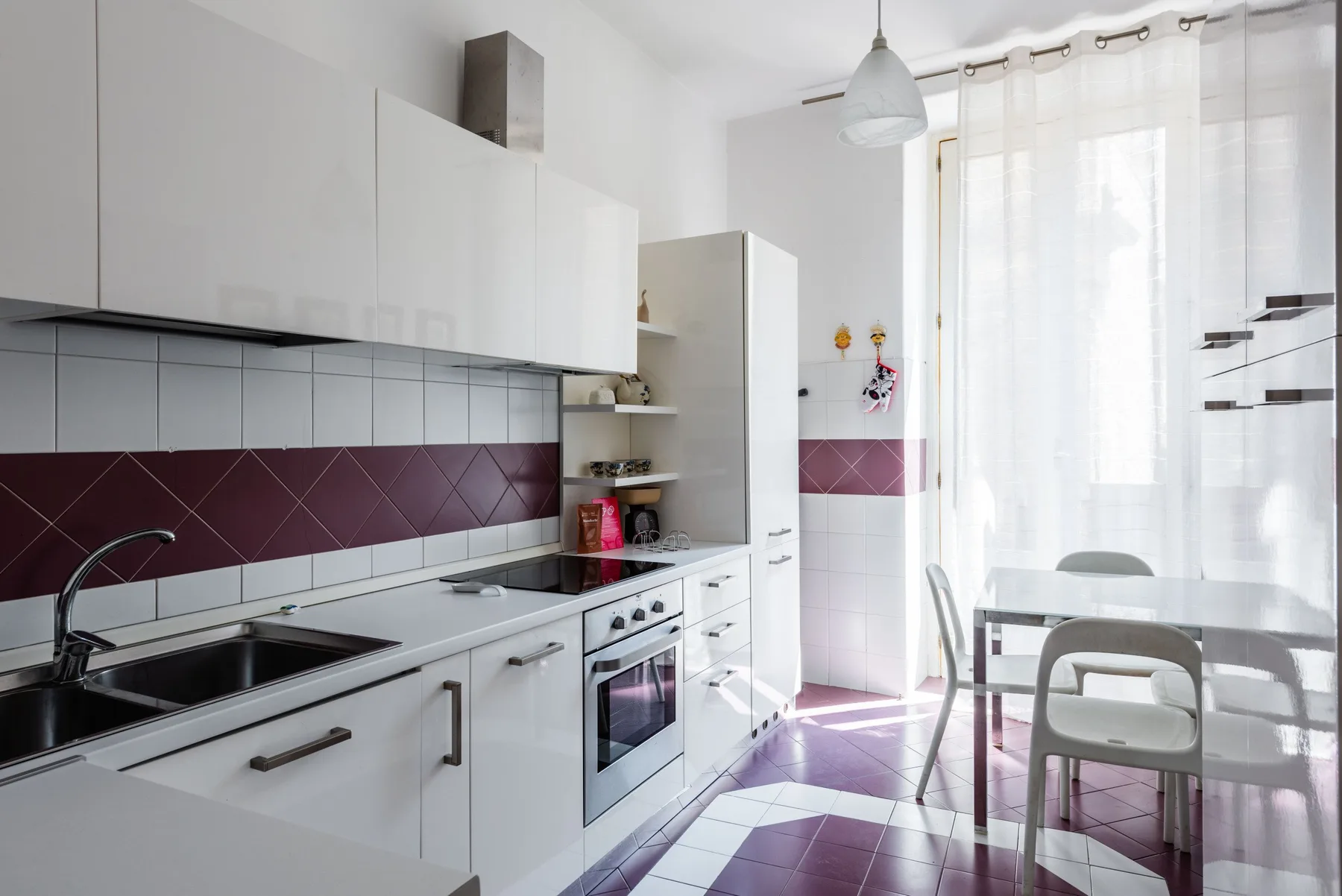 A bright kitchen with white cabinets, a tiled backsplash, and a dining table by the window.
