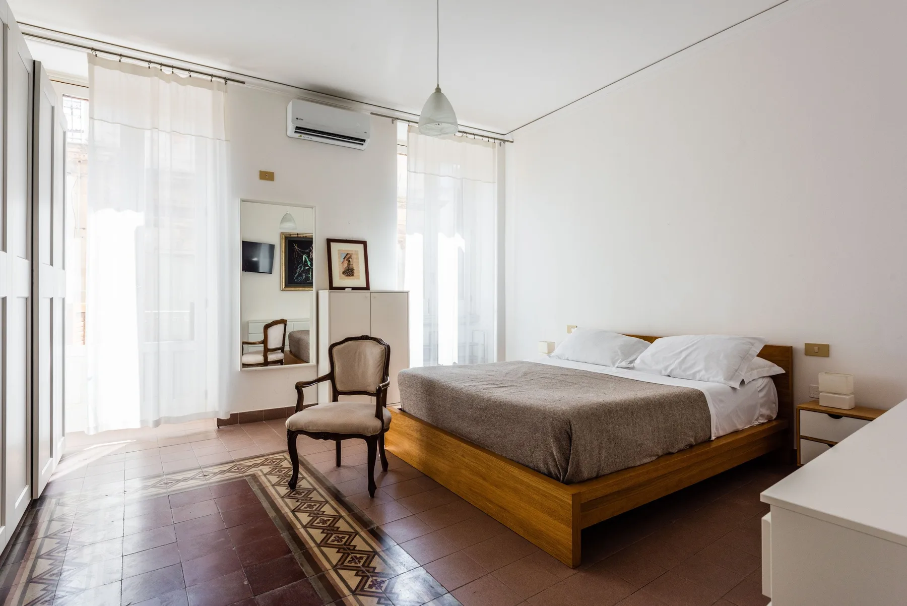 A bedroom with a bed, bedside tables, and tall windows with sheer curtains.